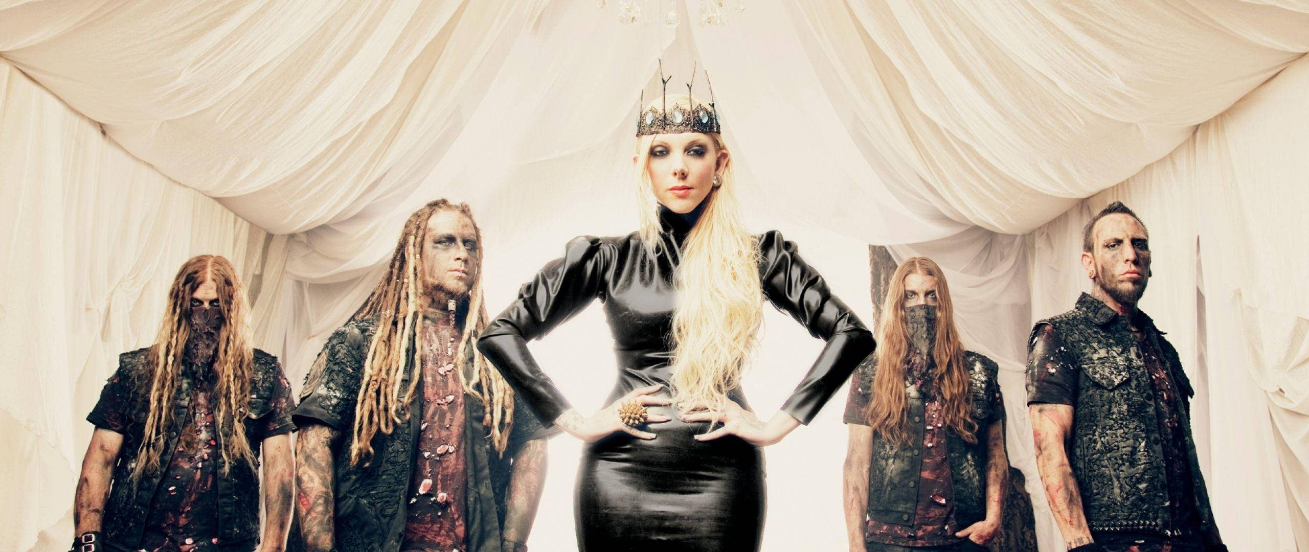 In This Moment《Blood》CD封面 壁紙 — 一個樂隊，中間有一位金髮女性穿著黑色皮裙和皇冠，自信地站立，被四位戴面具的樂隊成員包圍，上方有白色布料垂墜。