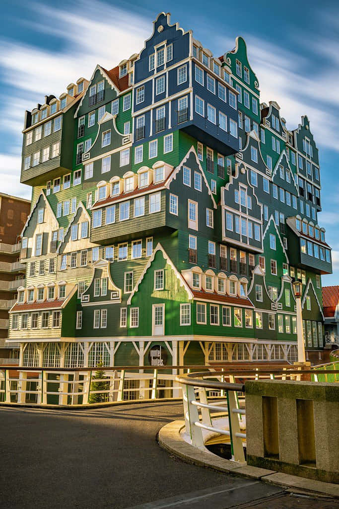 Inntel Hotel Zaandam 壯觀延時攝影 壁紙 — 一座高聳的現代建築，設計成類似堆疊的荷蘭山牆房屋，在明亮的藍天下擁有綠色和藍色的外牆。