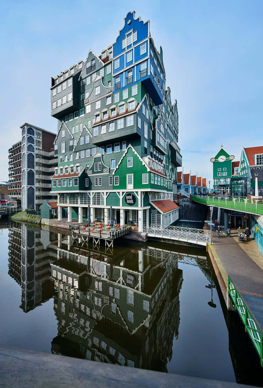 Inntel Hotel Zaandam 與池塘 壁紙 — 一座引人注目的現代建築，擁有綠色和藍色的荷蘭式山牆立面層疊，在晴朗的天空下完美地倒映在平靜的運河水中。