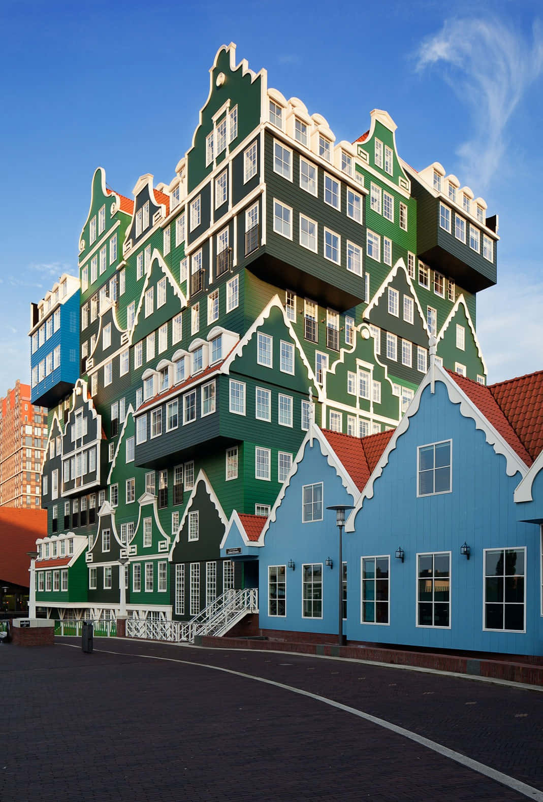 Inntel Hotel Zaandam 與道路 壁紙 — 一座引人注目的現代建築，設計成類似堆疊的荷蘭山牆房屋，綠色和藍色，在清澈的藍天下。