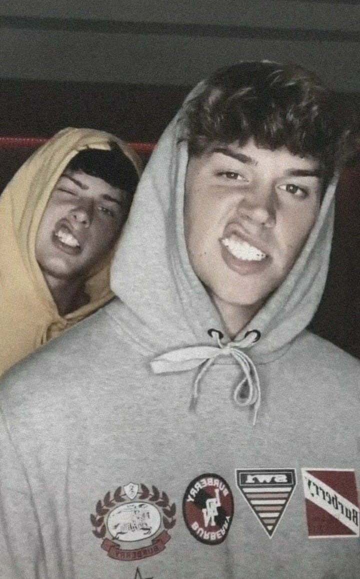 兩名身穿連帽衛衣的年輕男子在室內頑皮地咧嘴笑。