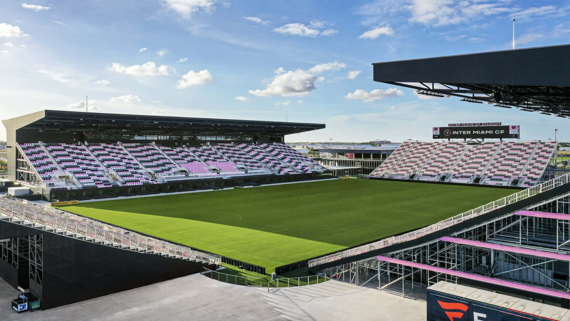Inter Miami FC 主場 DRV PNK 球場全景 壁紙 — 一個現代化的足球場，擁有充滿活力的綠色草坪和紫色座位，在明亮的藍天下有零星雲朵。
