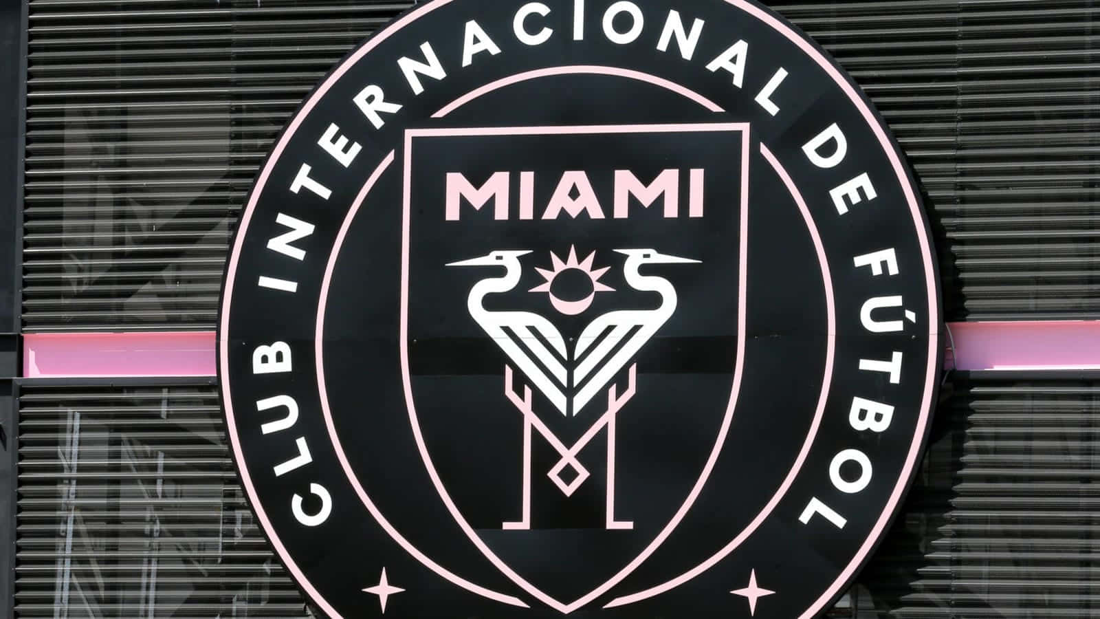 Inter Miami FC 官方隊徽極近拍攝 壁紙 — 現代建築外牆上粉紅色和黑色的 Club Internacional de Fútbol Miami 標誌特寫。