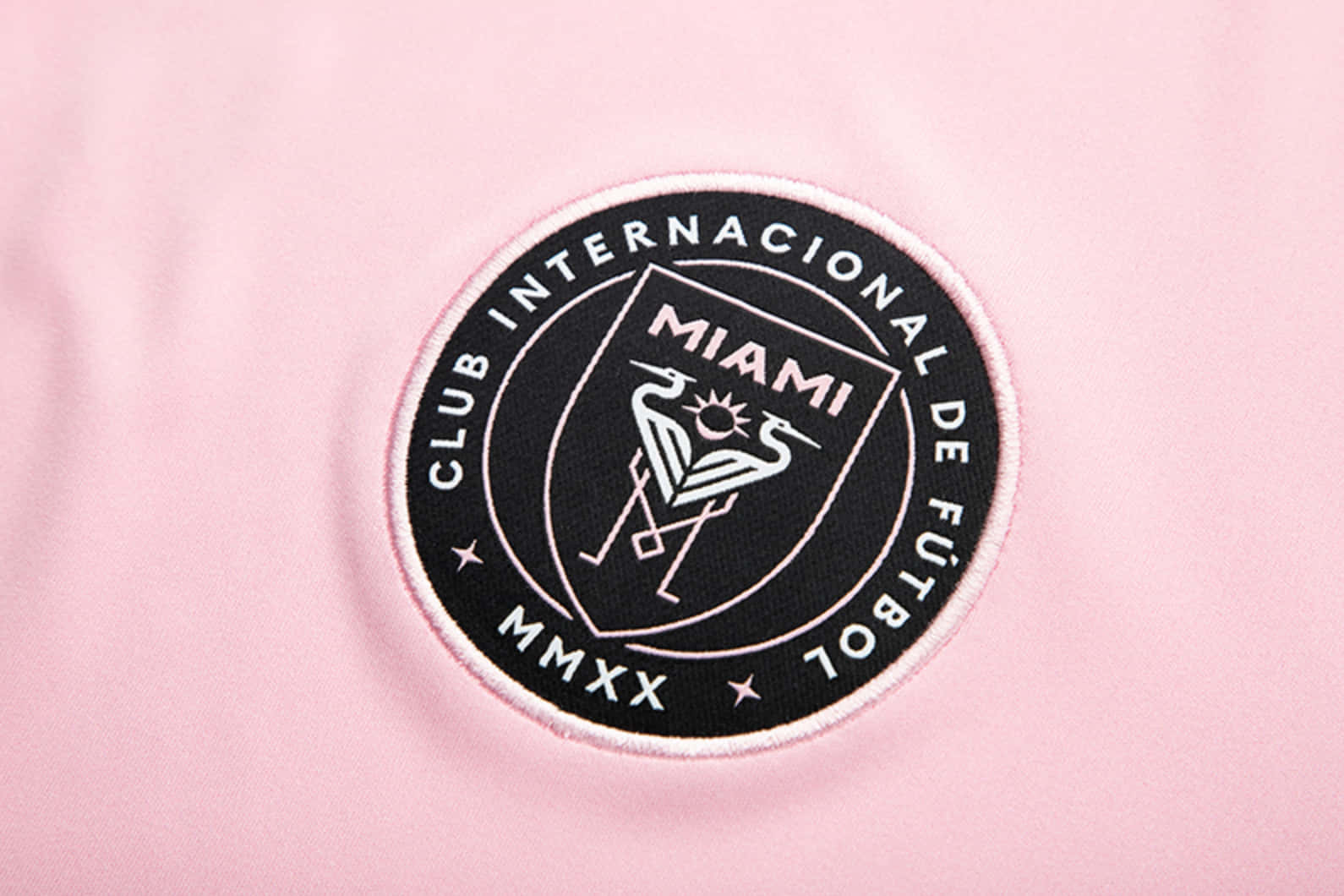 Inter Miami FC 粉紅標誌數位藝術 壁紙 — 柔軟粉紅色布料上黑白刺繡的邁阿密FC會徽特寫，可見針線紋理。