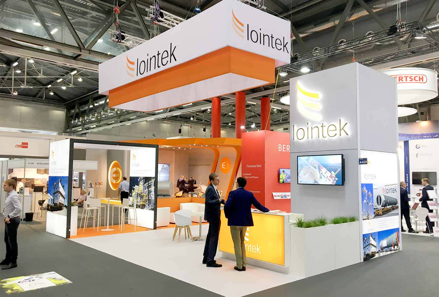 Exhibition 桌布 壁紙 — Iointek 的現代貿易展攤位，採用橙白色品牌設計，參觀者在明亮的展廳燈光下與顯示屏互動。