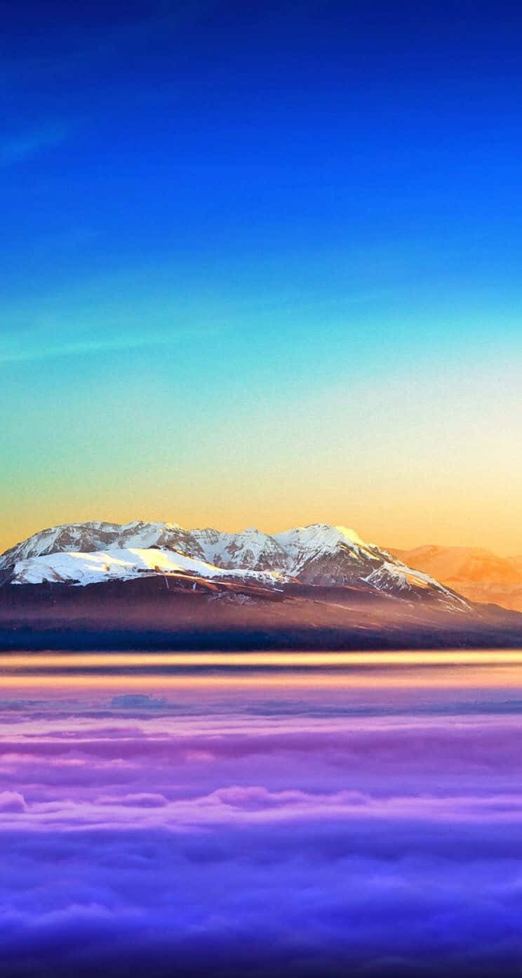iOS 1 彩色山峰懸於天際 壁紙 — 積雪的山峰在藍橙漸變的天空下，從紫色雲海中升起。