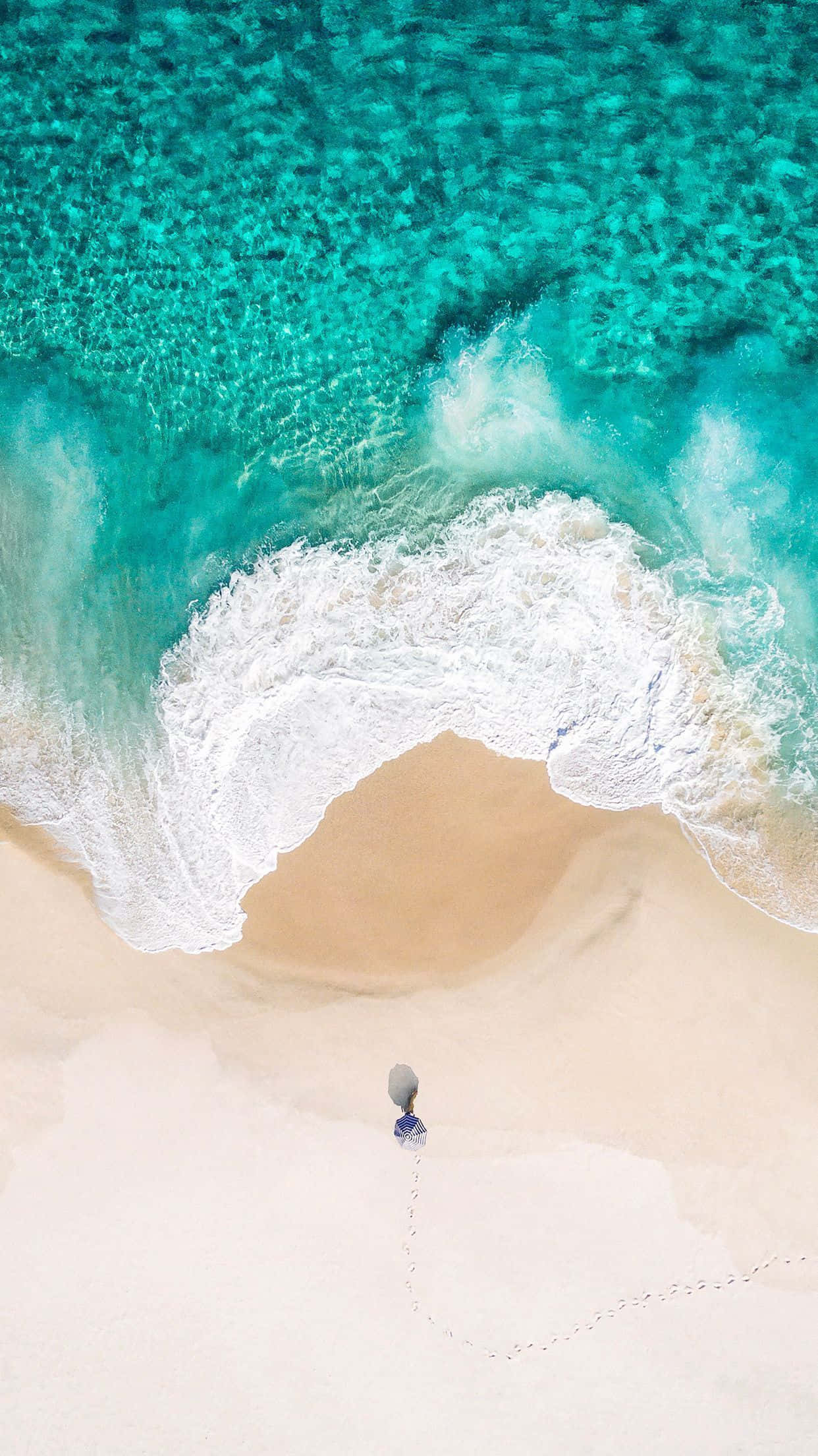 iOS 1 淺藍清澈海浪 壁紙 — 從空中俯瞰，一個人獨自走在純淨的白沙上，碧綠色的海浪翻滾而來。