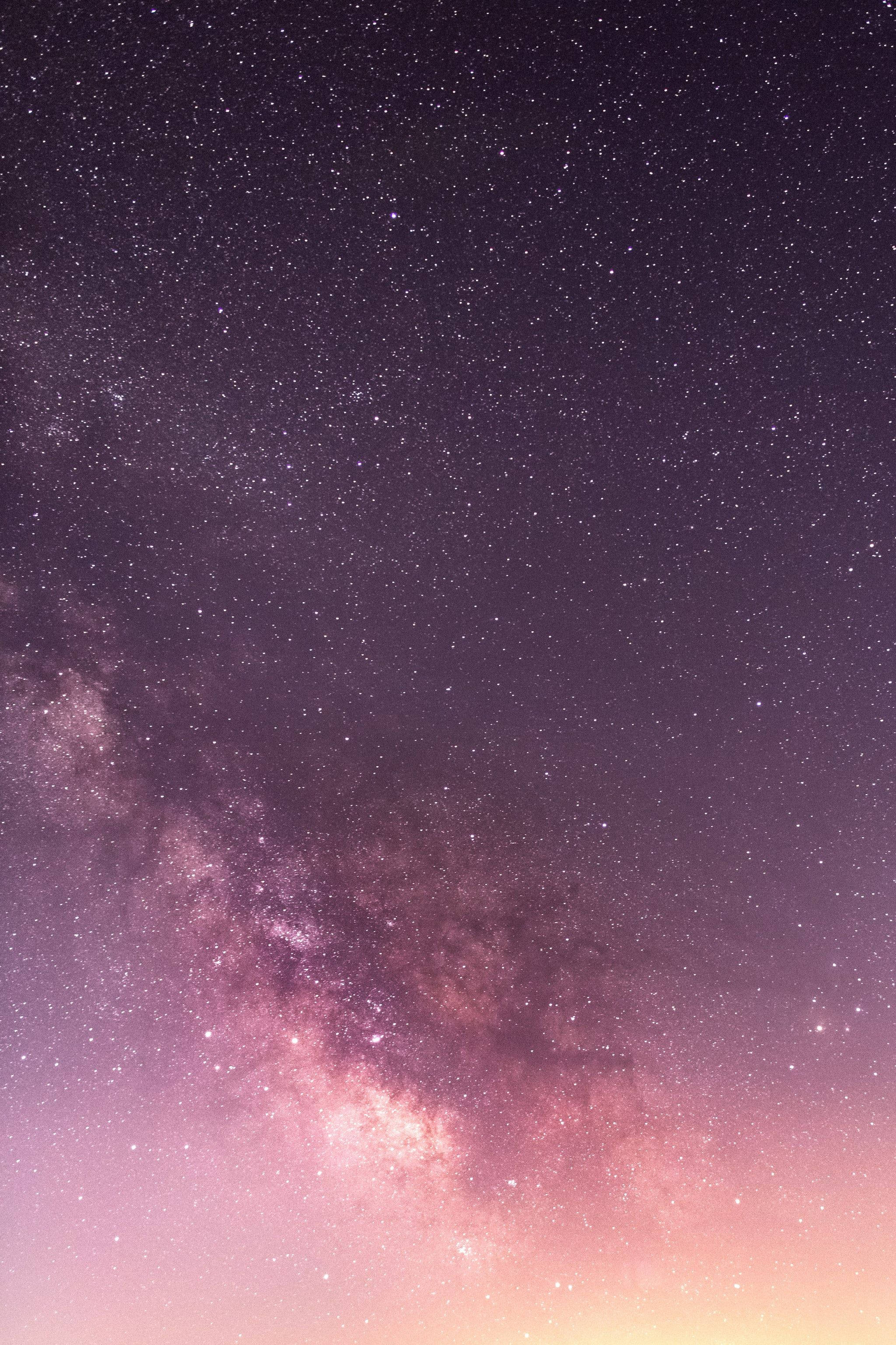 iOS 14 紫色夜空 壁紙 — 令人嘆為觀止的銀河系景觀，在繁星點點的夜空中散發出鮮豔的紫色和粉紅色光芒。