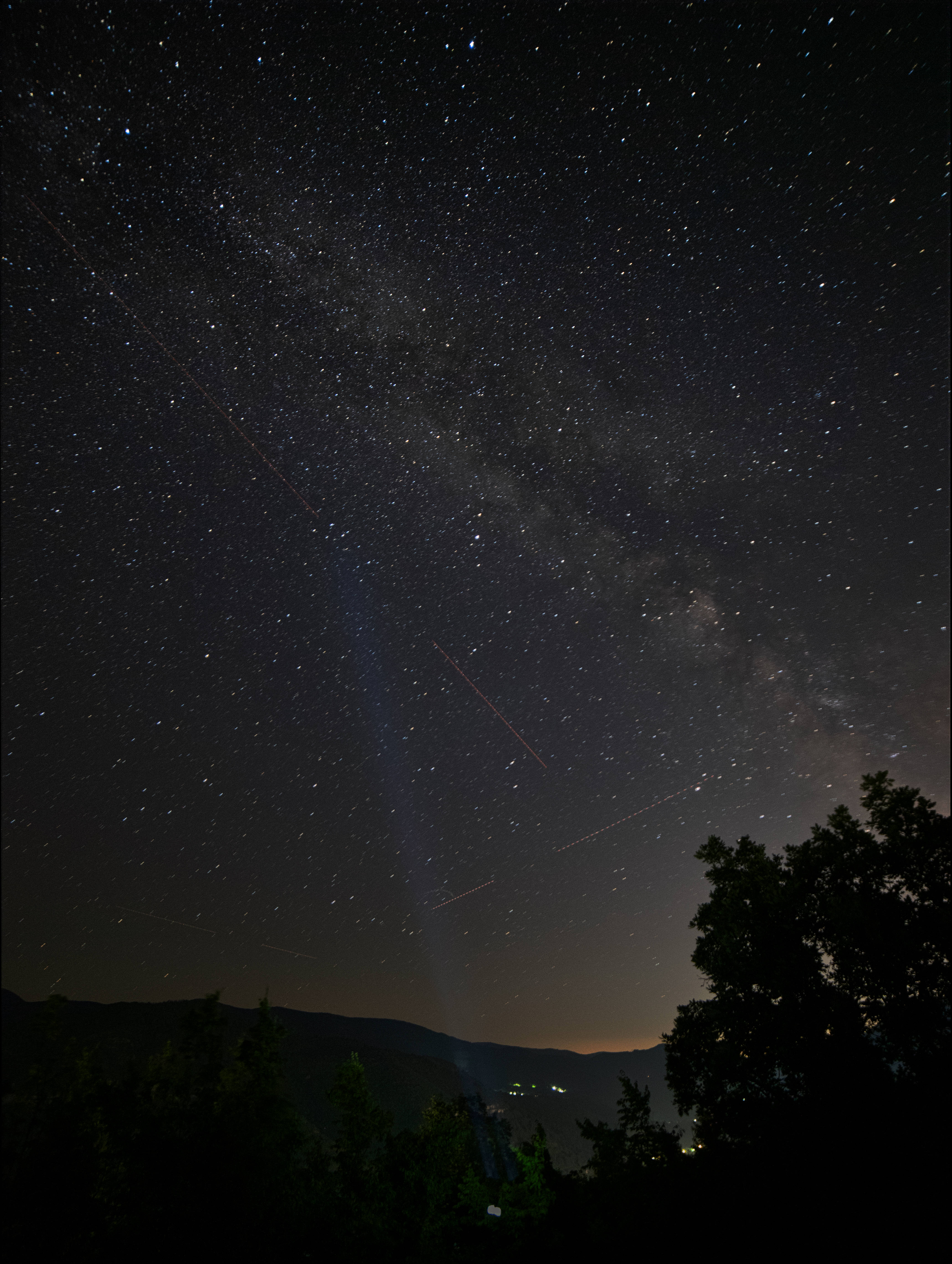 iOS 16 星空夜景 壁紙 — 繁星點點的夜空，銀河在剪影般的樹木和遠山之上拱起，籠罩在黑暗天鵝絨般的廣闊空間中。