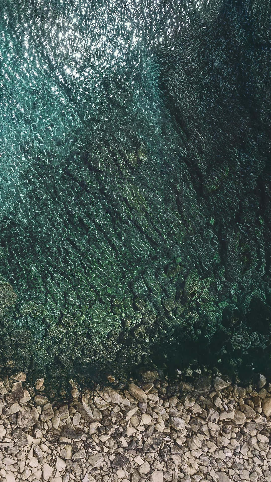 平靜海岸線上，清澈碧綠的海水在陽光照耀的岩石上泛起漣漪。
