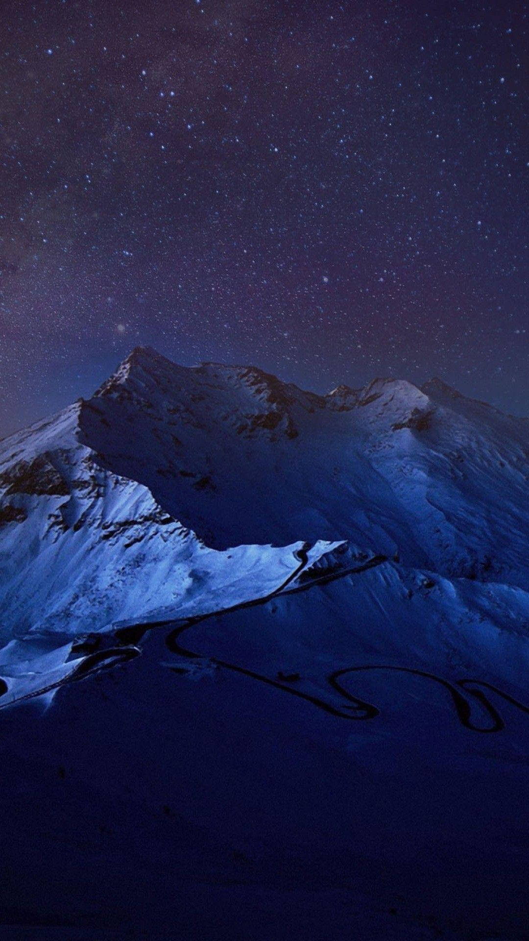 iOS 8 藍色阿爾卑斯山 壁紙 — 一條蜿蜒的道路在繁星點點的紫色夜空下蜿蜒穿過積雪覆蓋的山脈。