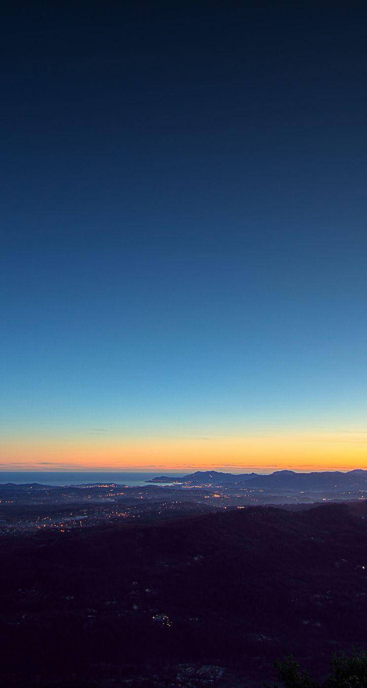 iOS 8 夕陽 壁紙 — 海岸城市上空的壯麗暮色景觀，下方燈光閃爍，天空從深藍漸變到溫暖的橙色。