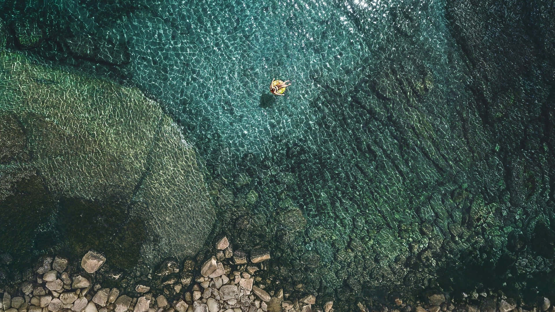 一個人在清澈碧綠的海水中漂浮，下方可見岩石。
