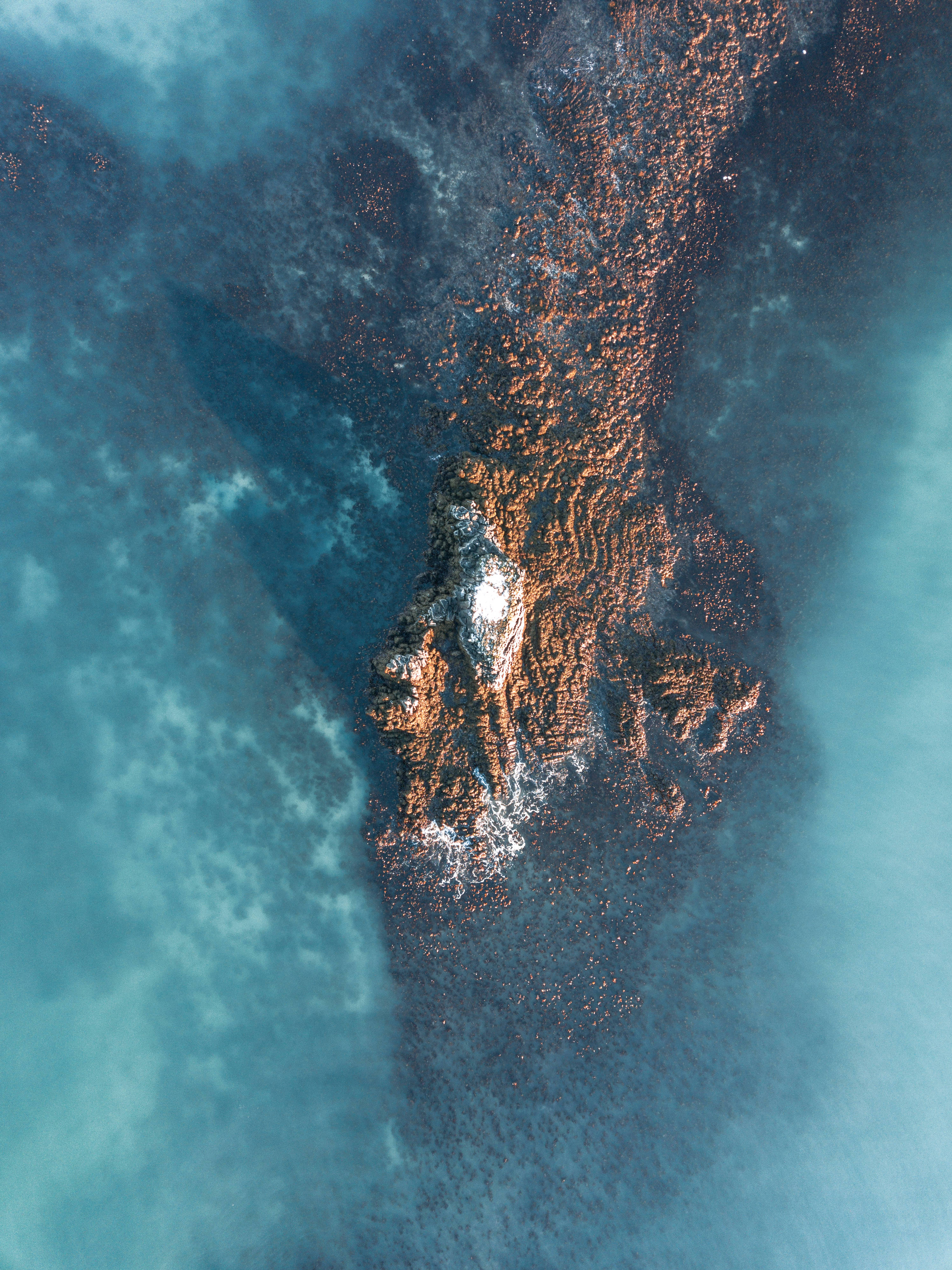 岩石島嶼 iPad 壁紙 — 崎嶇山峰的鳥瞰圖，山頂積雪，周圍是帶紋理的藍色和橙色地形。