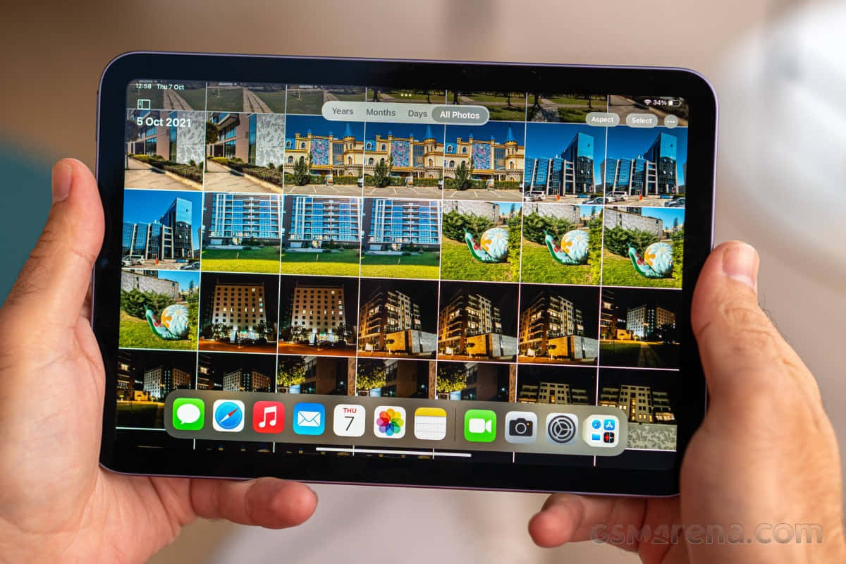 iPad Mini OLED畫面 壁紙 — 雙手拿著平板電腦，顯示現代建築和雕塑在明亮日光下的照片庫。