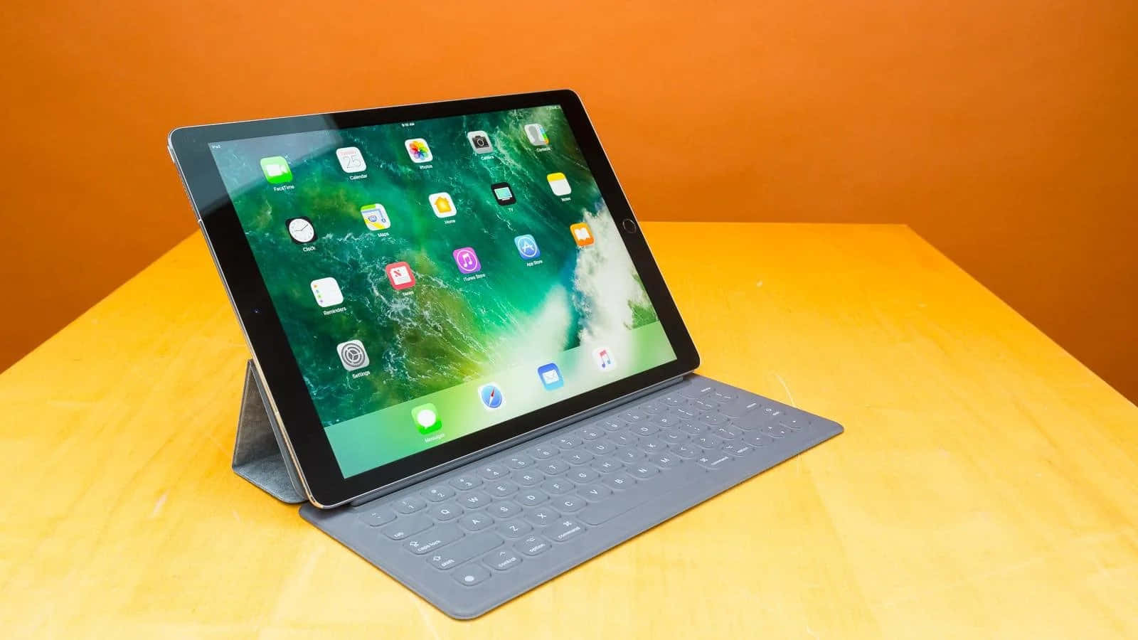 手持 iPad，背景為花卉圖案布料 壁紙 — 一部配備鍵盤保護套的時尚平板電腦放在木桌上，背景是溫暖的橙色牆壁。