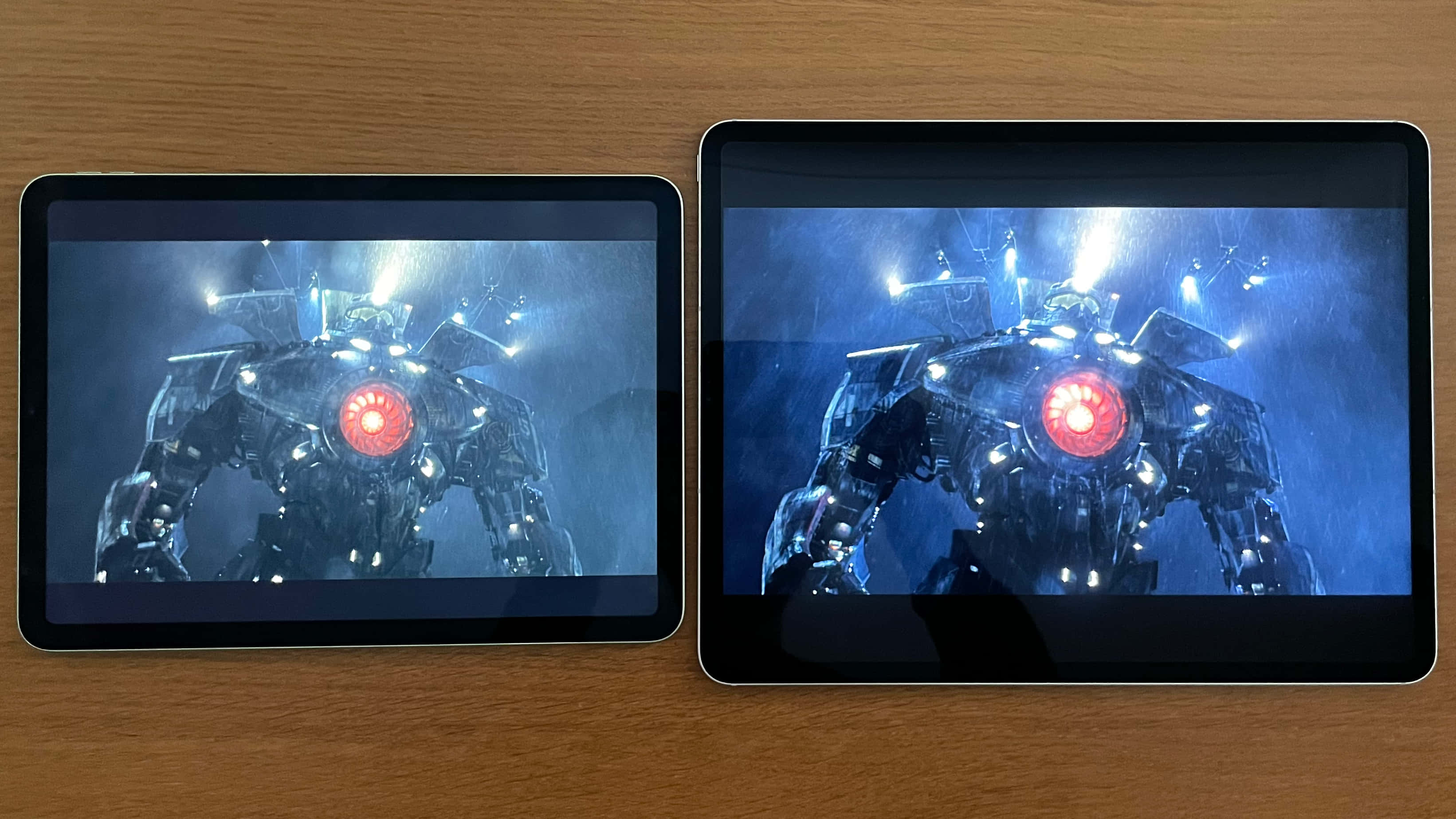 iPad OLED畫面 壁紙 — 兩個平板電腦在木質表面上顯示一個高聳的機械人，在戲劇性的藍色燈光下有一隻發光的紅色眼睛。