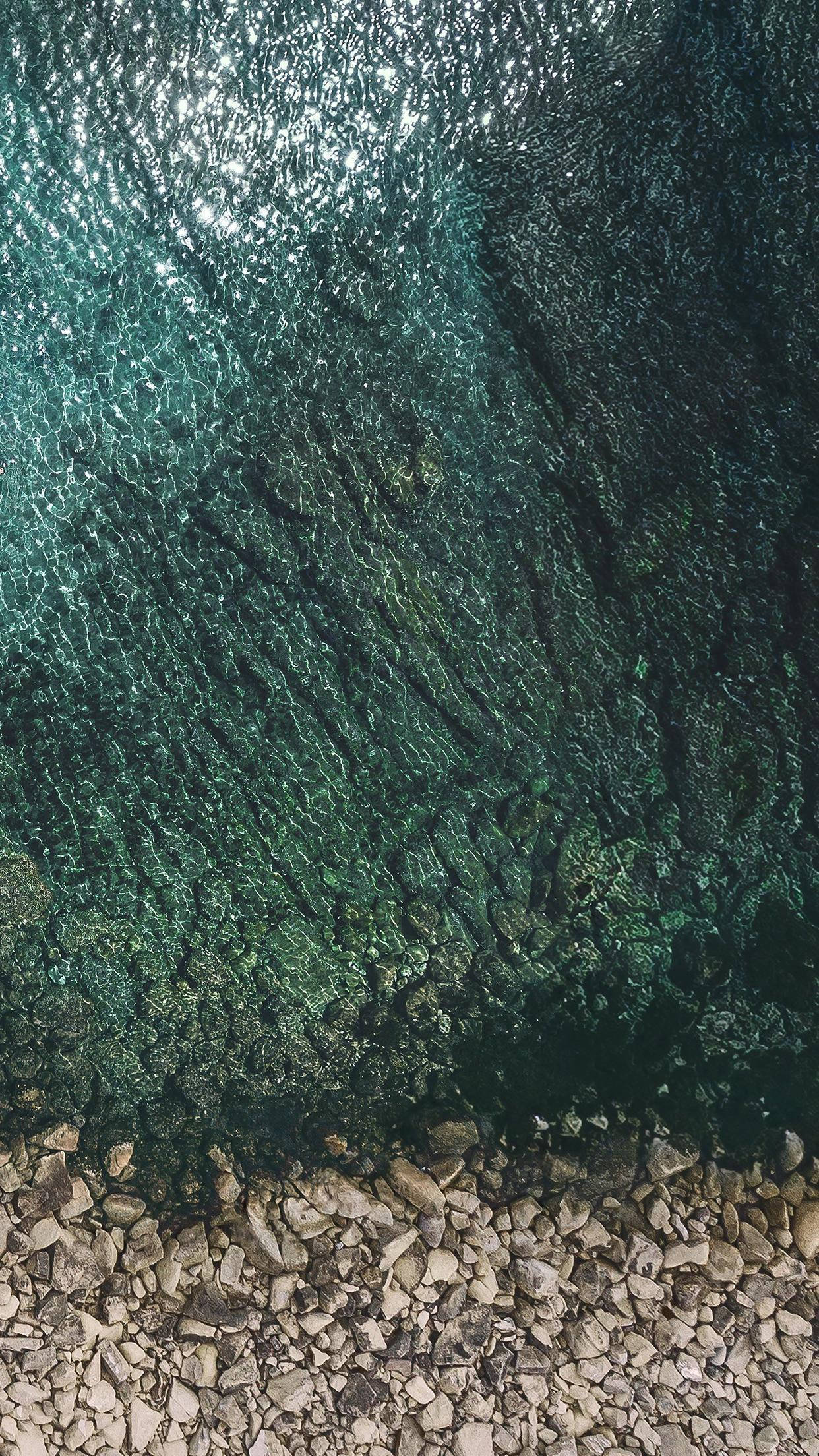 iPad Pro 岩石海岸旁的清澈海水 壁紙 — 俯瞰清澈碧綠的海水在岩石海岸線上泛起漣漪，陽光在水面上閃爍。