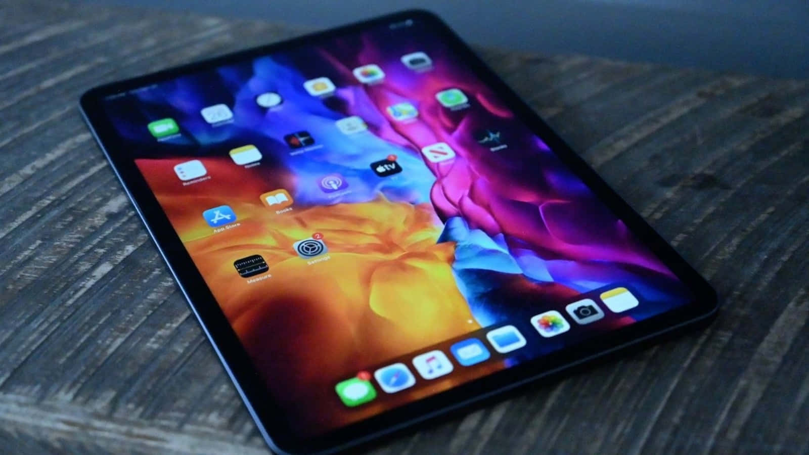 一位男士使用最新款iPad 壁紙 — 一部時尚平板電腦，帶有鮮豔的抽象壁紙，放置在紋理木質表面上。