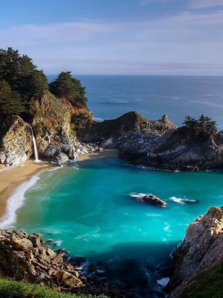麥威瀑布自然 iPad 壁紙 — 一個令人驚嘆的海岸小海灣，擁有碧綠的海水、沙灘和從岩石懸崖傾瀉入海的瀑布。