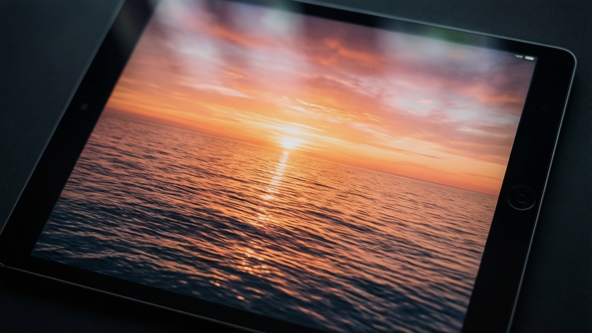 iPad 屏幕上的日出美景 壁紙 — 平板電腦顯示在平靜的海面上，金色的陽光反射在漣漪波紋上的鮮豔日落。