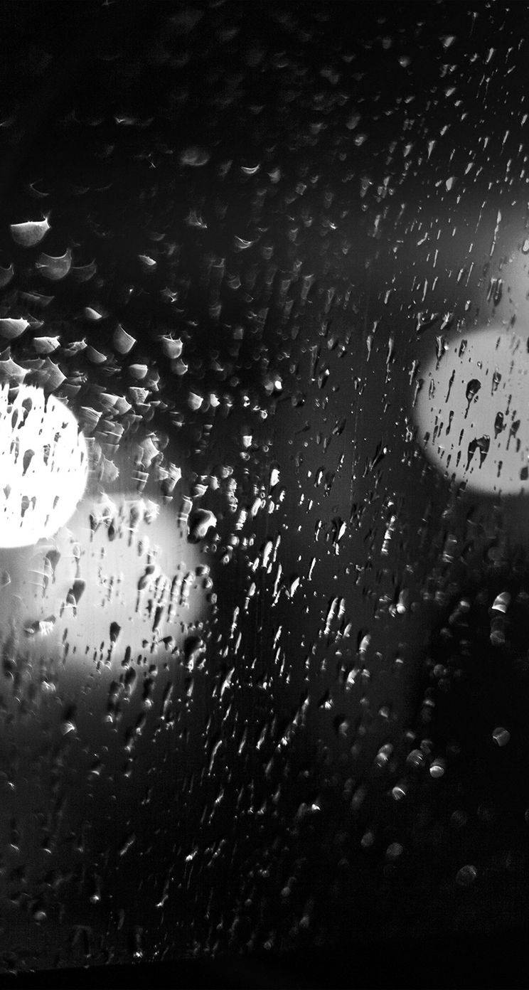 沉醉於 iPhone 雨天之美 壁紙 — 雨滴劃過黑暗的窗戶，將閃爍的城市燈光模糊成柔和的圓形散景。