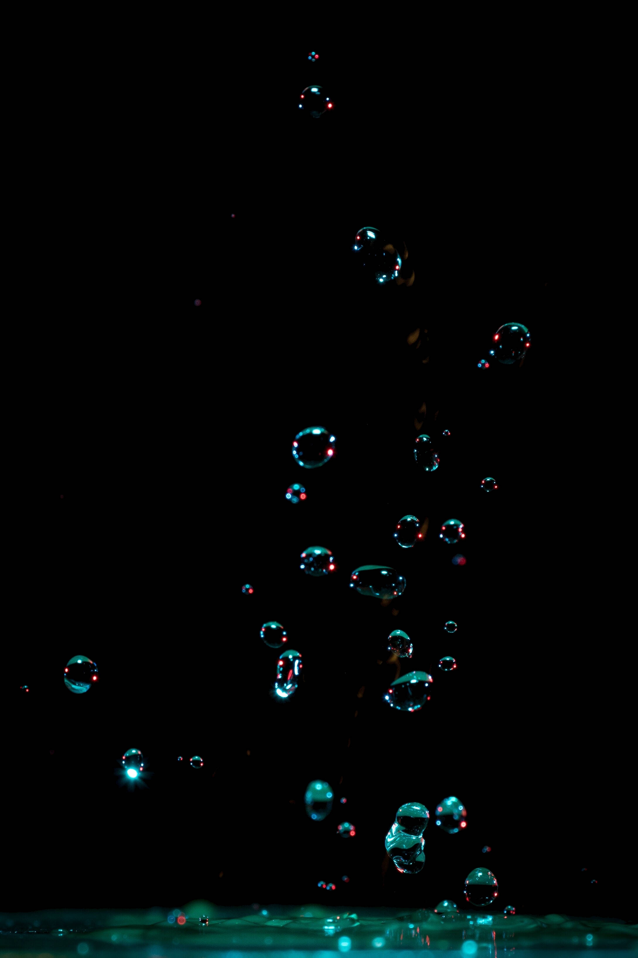 iPhone 11 Pro Max 水珠特寫 壁紙 — 在漆黑背景中懸浮的閃亮水滴，帶有發光的青綠色反射。