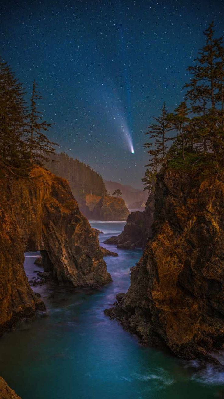 彗星劃過繁星點點的夜空，下方是岩石海岸的海灣，海水閃爍著藍光。