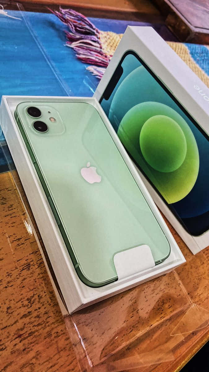iPhone 12：更快、更聰明、更堅固！ 壁紙 — 一部薄荷綠色的iPhone 12放在打開的盒子裡，置於木桌上，旁邊有色彩繽紛的編織布料。