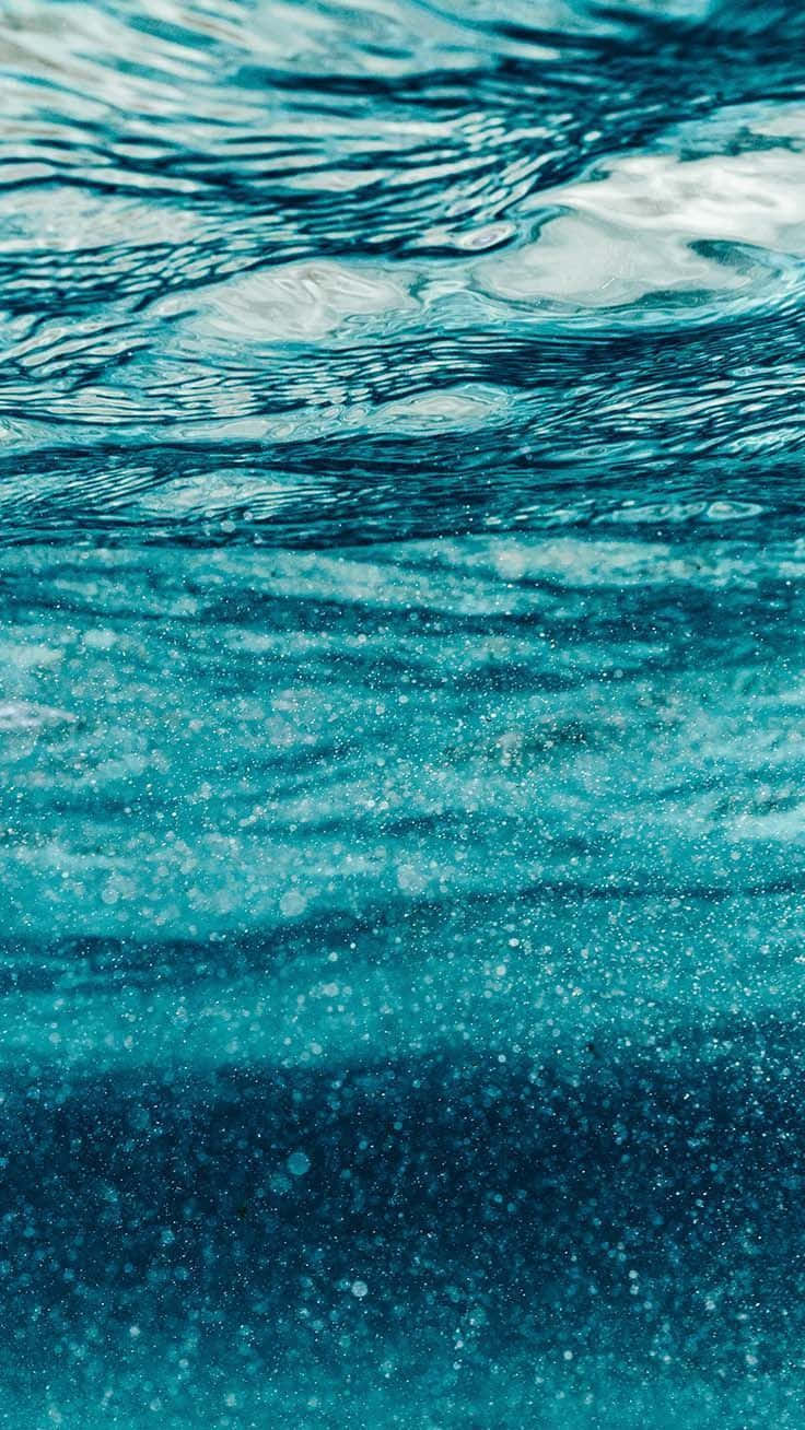 以時尚青綠色 iPhone 獲得眾人目光 壁紙 — 水下視角，波光粼粼的碧綠海水，光線穿過水面，形成閃爍圖案。