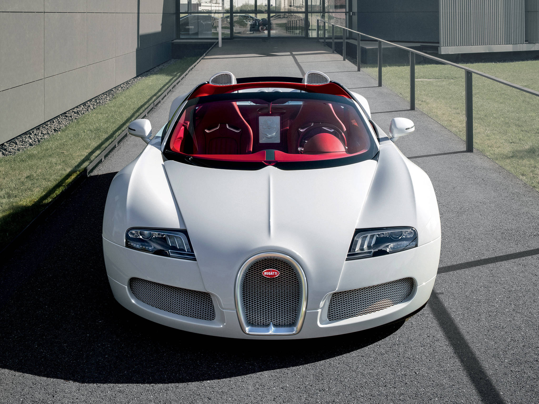 白色布加迪威龍正面 iPhone 壁紙 — 一輛純白色的Bugatti Veyron Grand Sport開篷車，紅色內飾，停泊在現代化鋪砌的車道上，在明亮的日光下。