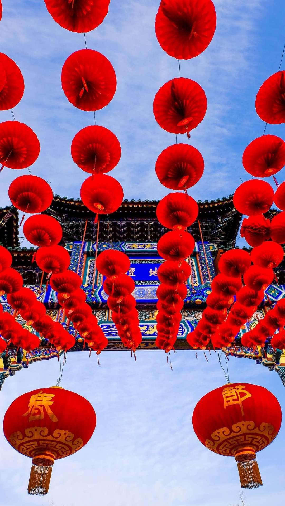 以iPhone慶祝中國新年！ 壁紙 — 鮮豔的紅色燈籠如瀑布般懸掛在晴朗的藍天下，上方是華麗的傳統中式大門。