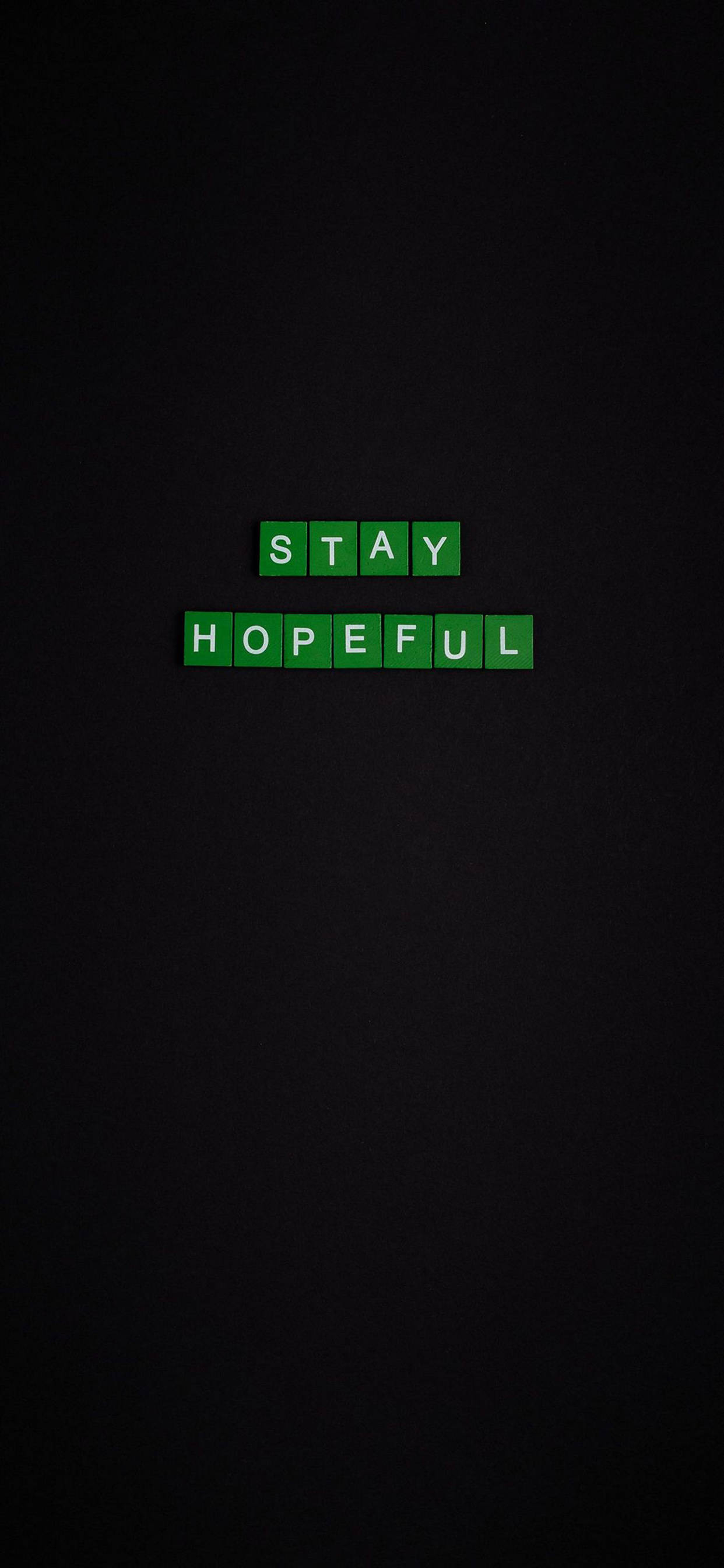 保持希望勵志 iPhone 壁紙 — 綠色拼字磚塊拼出 stay hopeful，居中放置在深色紋理背景上。