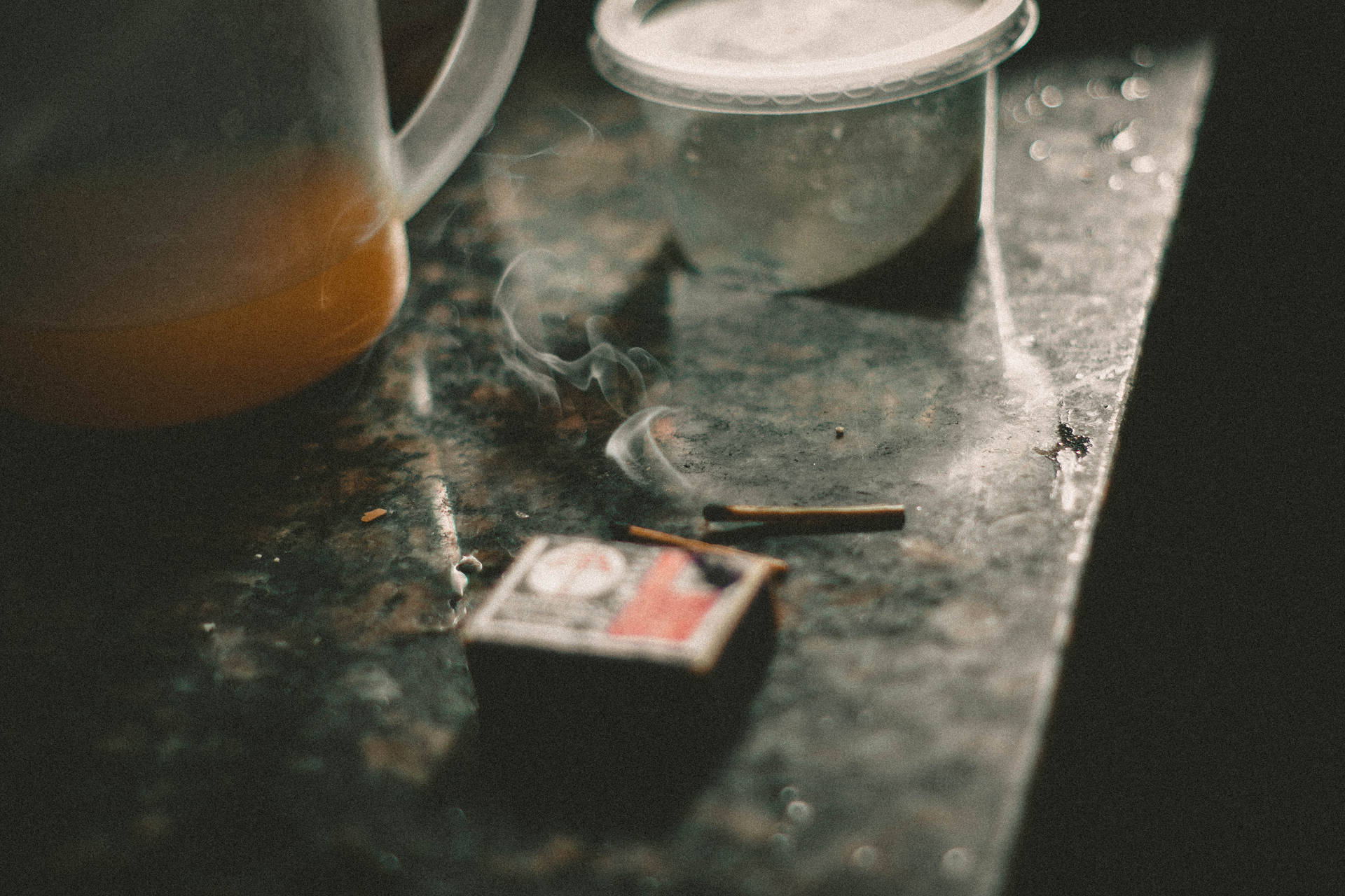 一根點燃的火柴在深色檯面上悶燒，旁邊有一個裝著橙色液體的壺。 — iPhone 4K 壁紙 壁紙
