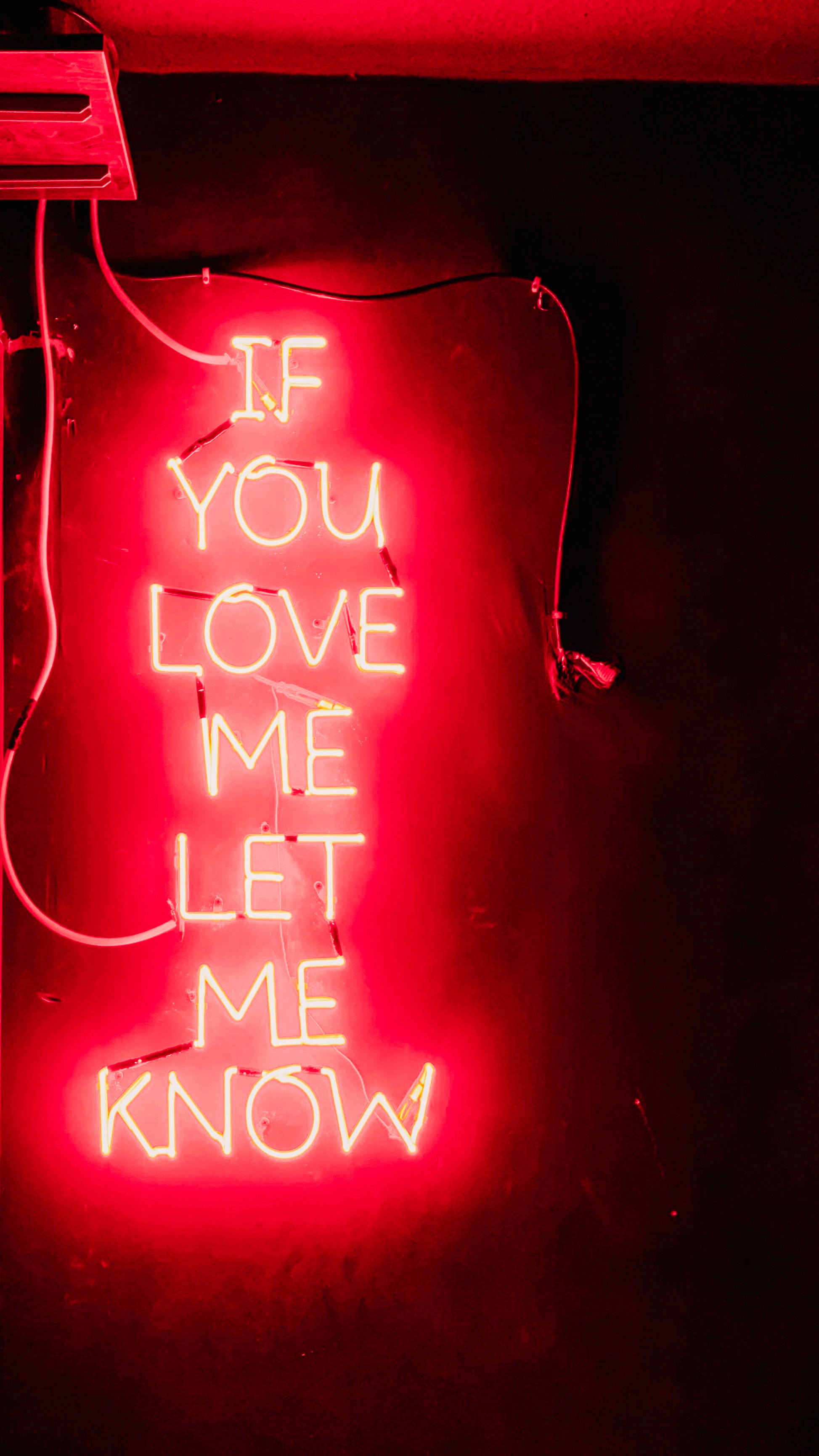 紅色霓虹標語 iPhone 6 壁紙 — 一個發光的紅色霓虹燈牌寫著 'IF YOU LOVE ME LET ME KNOW'，映在昏暗空間的深色牆上。