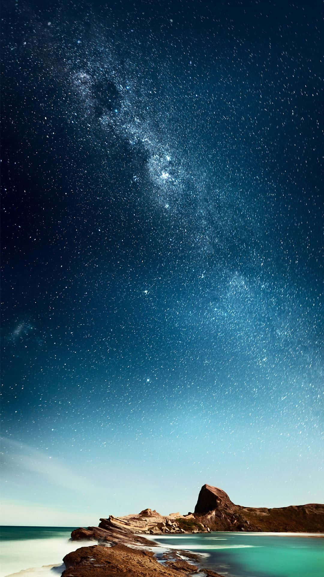 夜晚，銀河系在岩石海岸和碧綠海水上方。