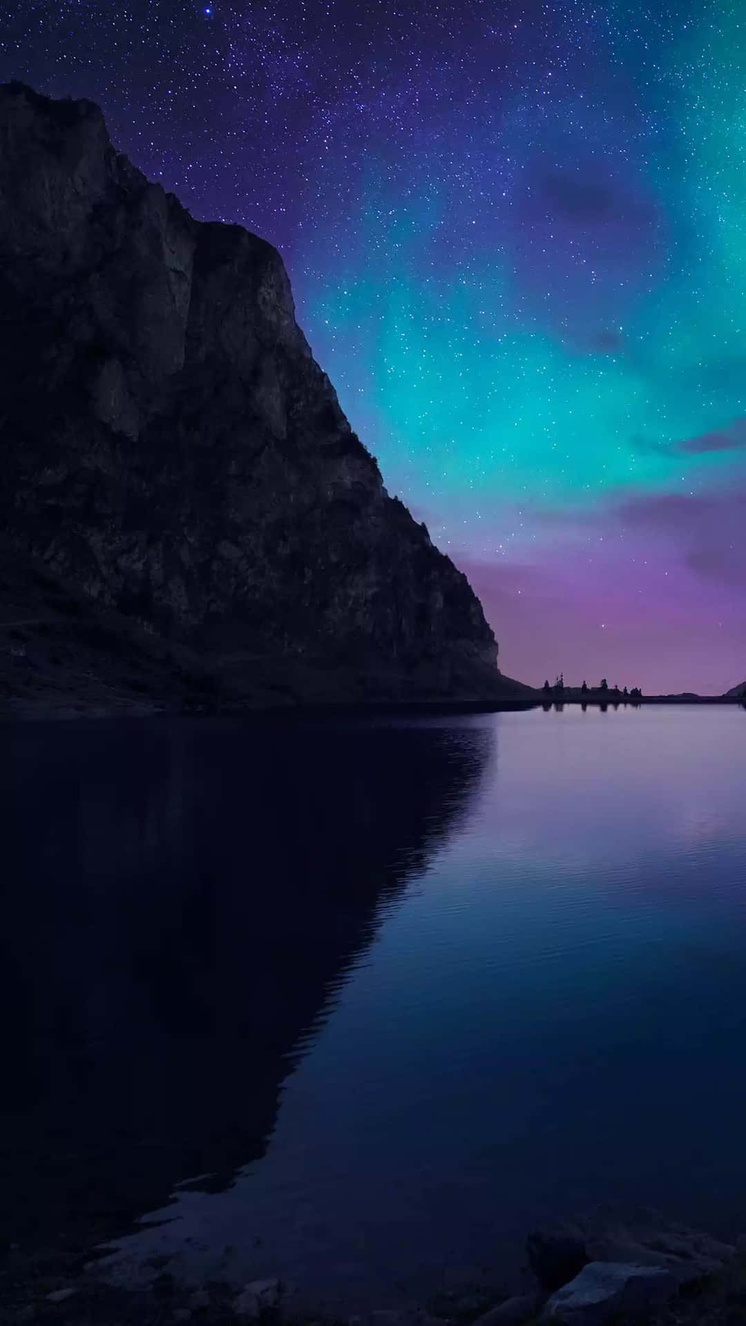 夜晚，北極光和星星倒映在岩石峭壁旁的平靜湖面上。