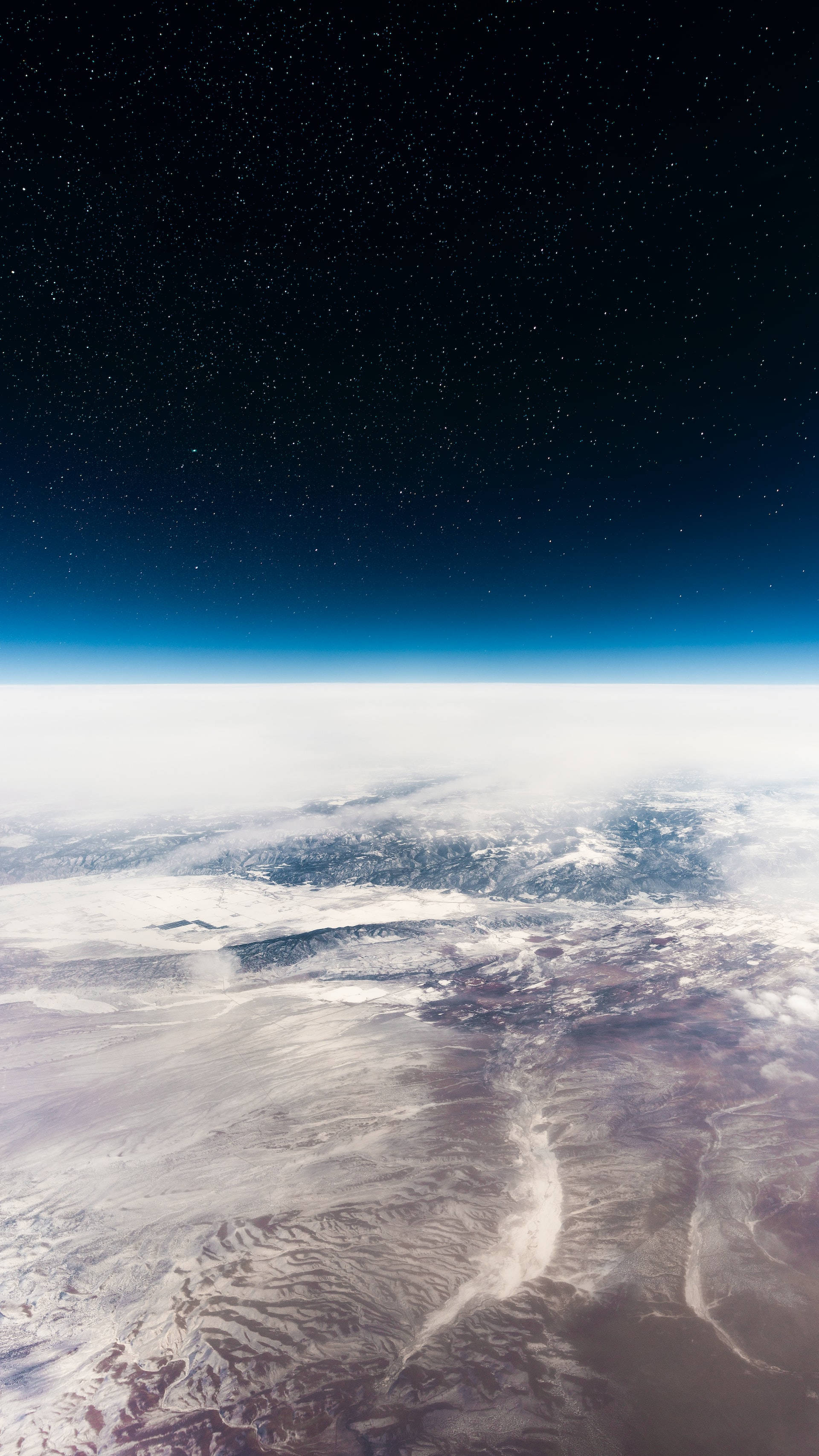 地球大氣層 iPhone 6 壁紙 — 從太空俯瞰地球的壯麗景色，展現出星夜天空籠罩著旋轉的雲層和覆蓋著白雪的地形。