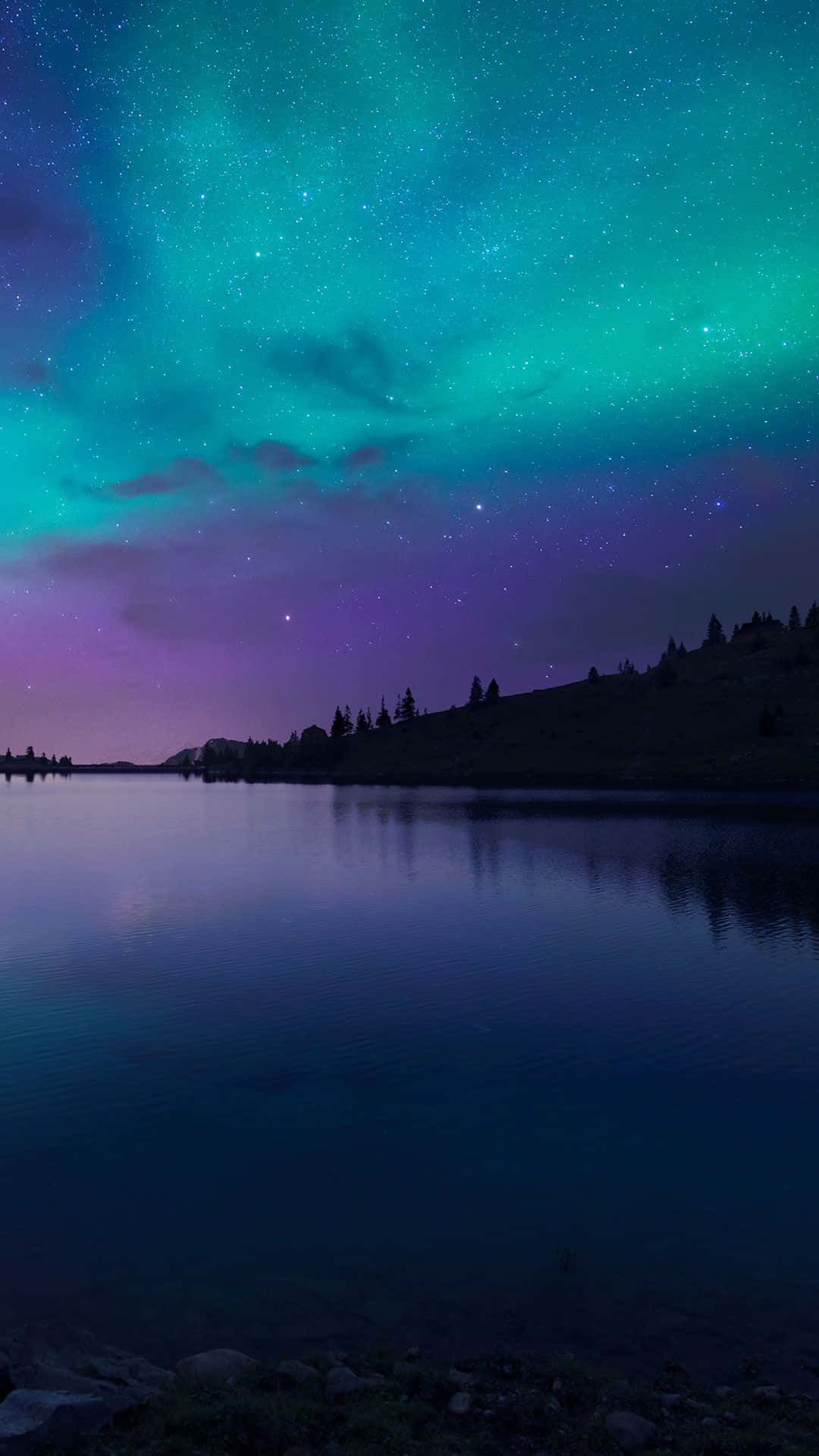 iPhone 6s 預設壁紙：夜空湖景 壁紙 — 北極光在電光藍綠和紫色中舞動，映照在平靜的湖面上，周圍是剪影般的山丘，夜空繁星點點。