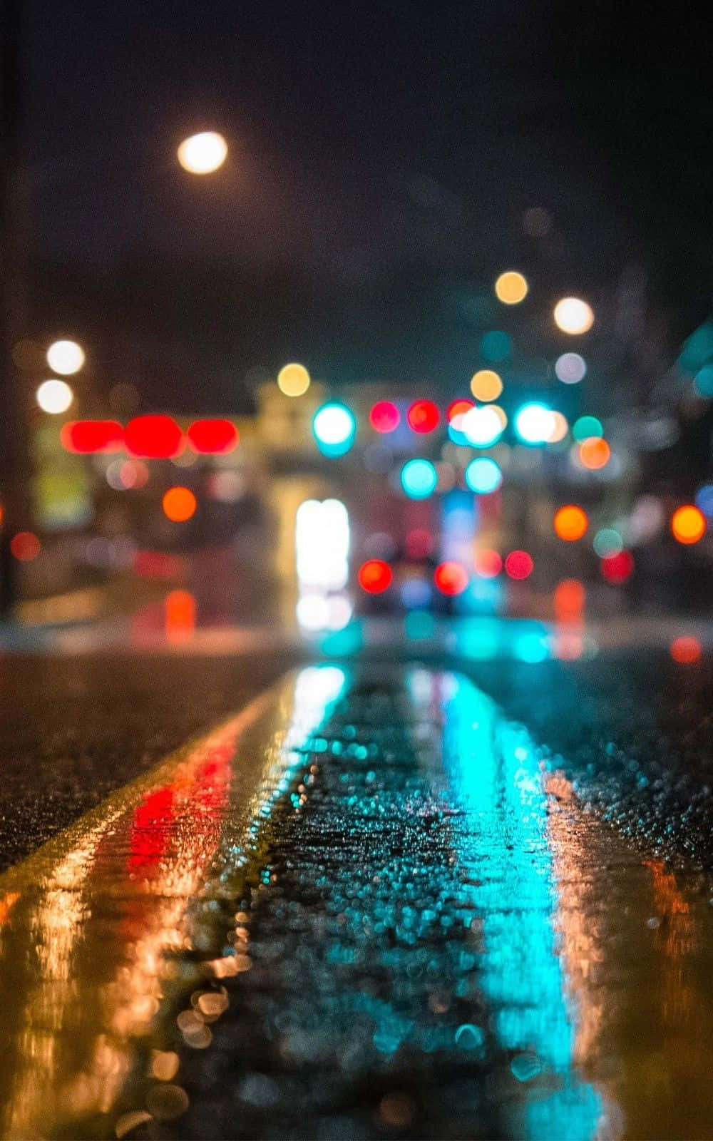 iPhone 6s 預設街景壁紙 壁紙 — 雨夜濕滑的城市街道，發光的散景燈光在濕漉漉的瀝青上反射。