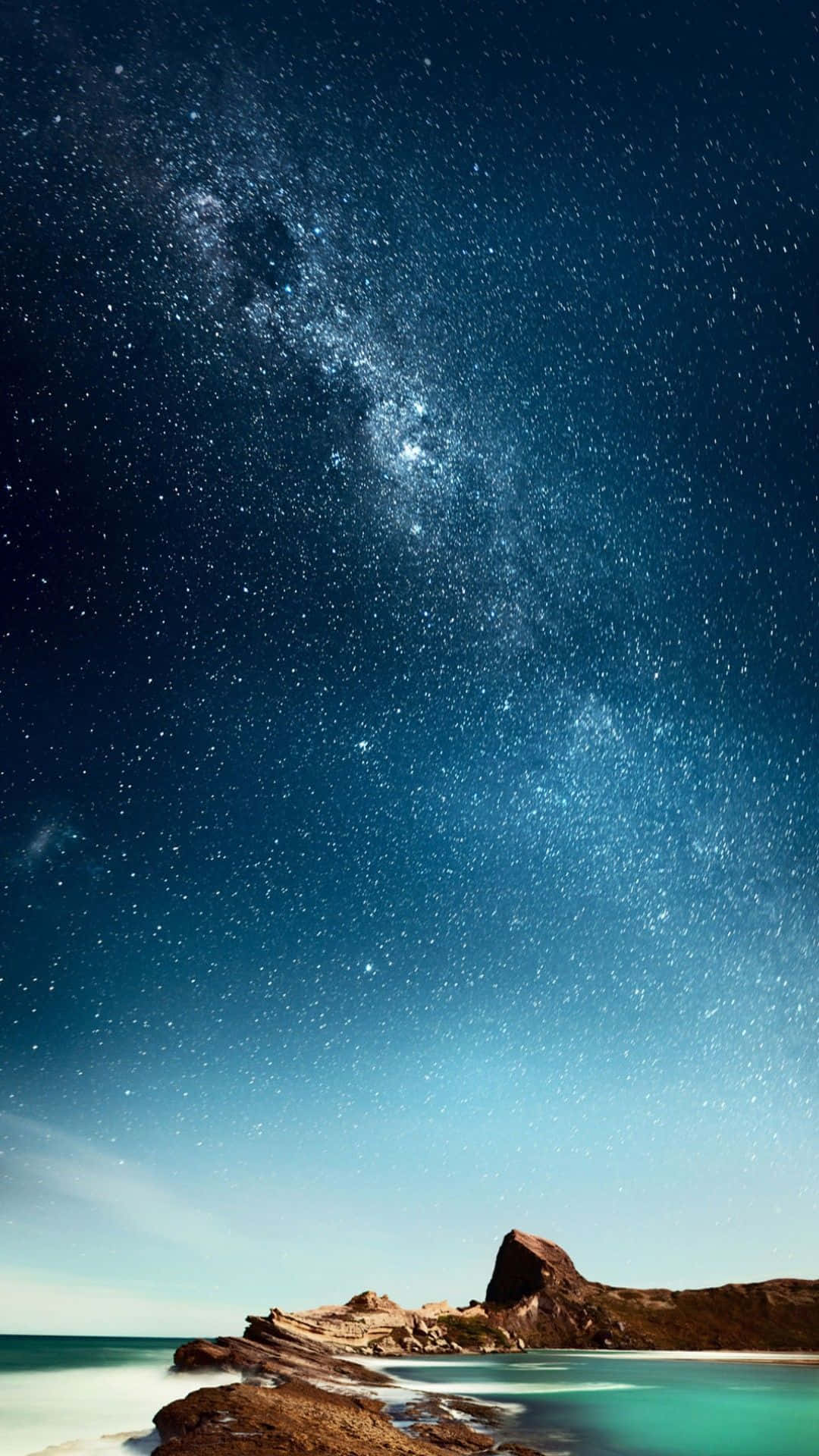 夜晚，銀河系在平靜的海洋和岩石海岸上空。