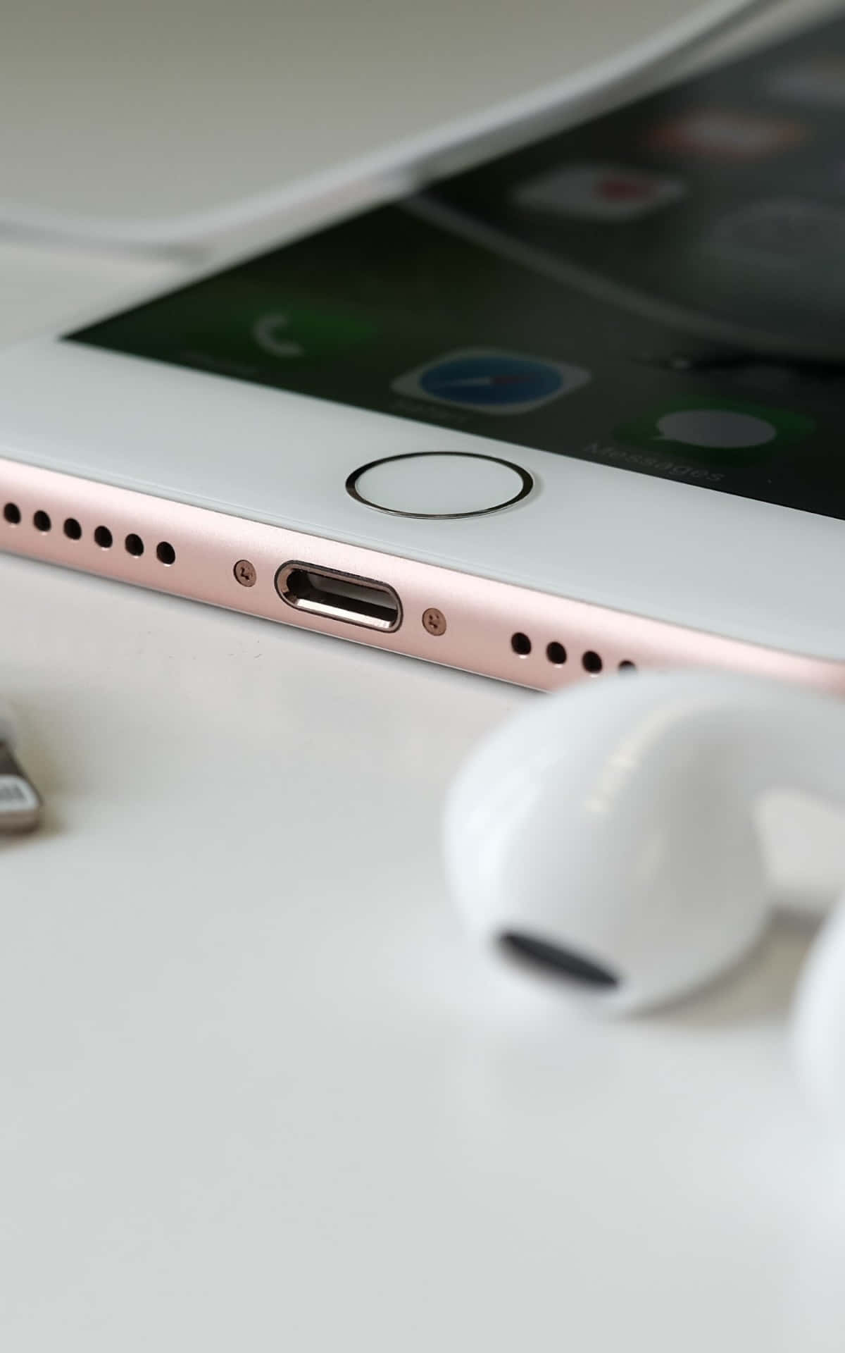 玫瑰金iPhone配白色耳機放在白色桌面上。