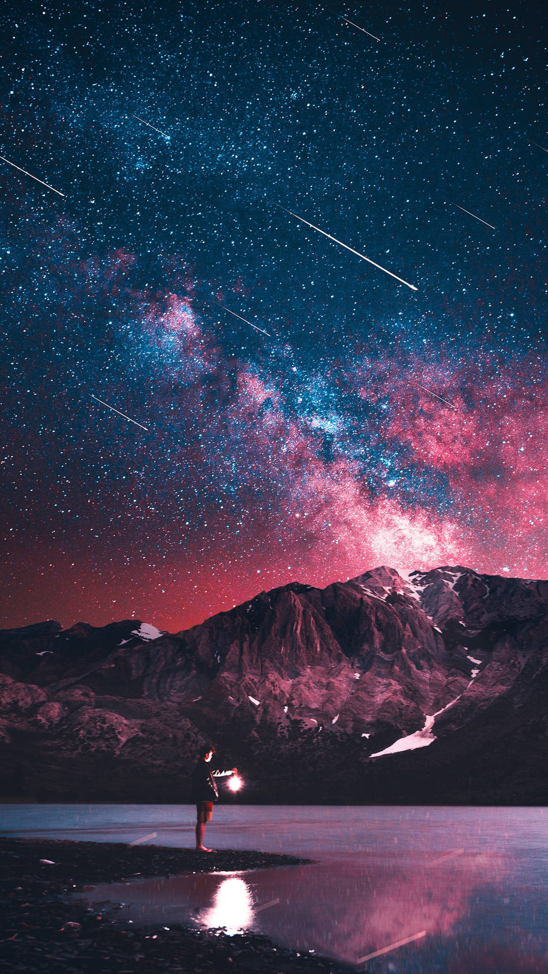 一個人在湖岸邊舉著燈光，星空下，背景有山脈