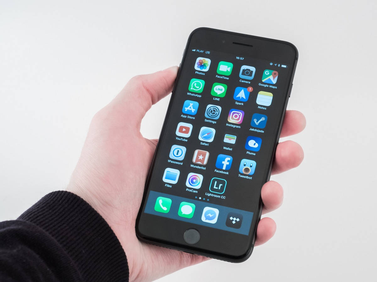 iPhone 8 螢幕 壁紙 — 一隻手拿著一部黑色智能手機，屏幕上顯示彩色應用程式圖標的網格，背景為純白色。