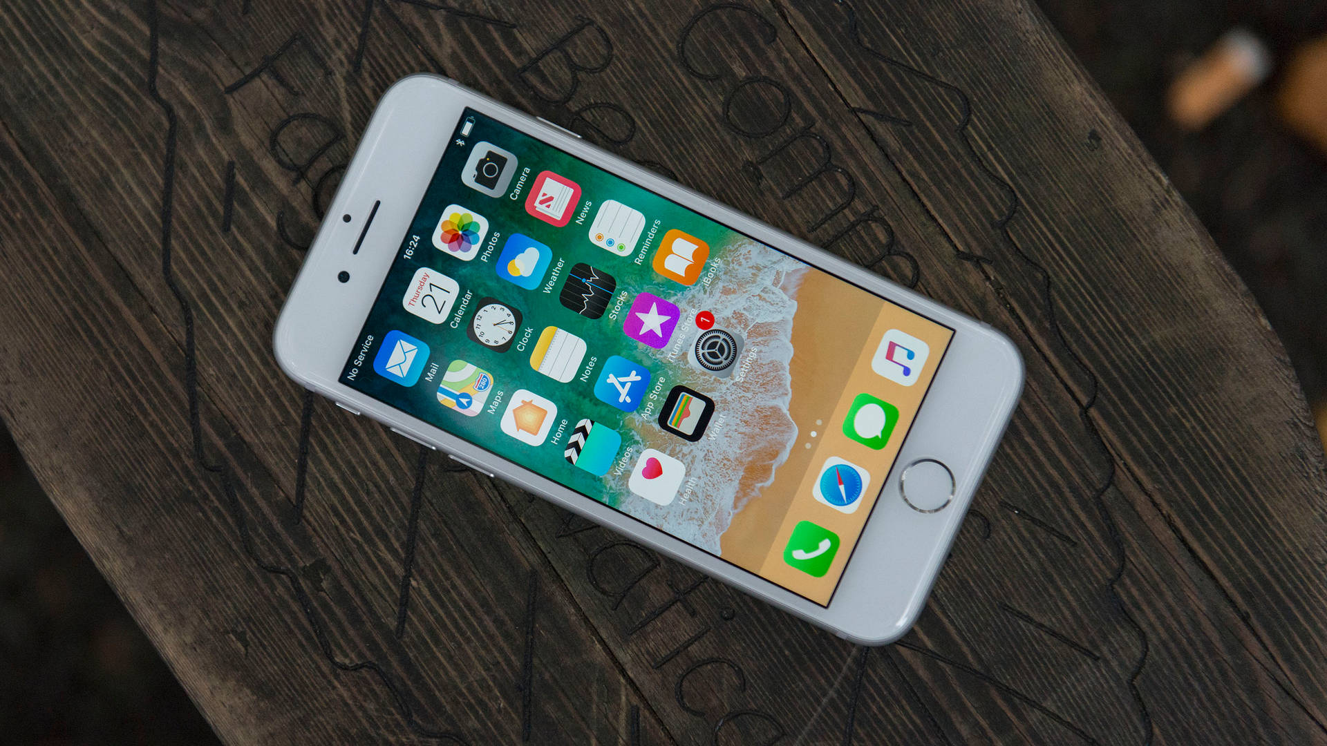 白色 iPhone 6s 在木桌上顯示主屏幕及應用程式圖示。