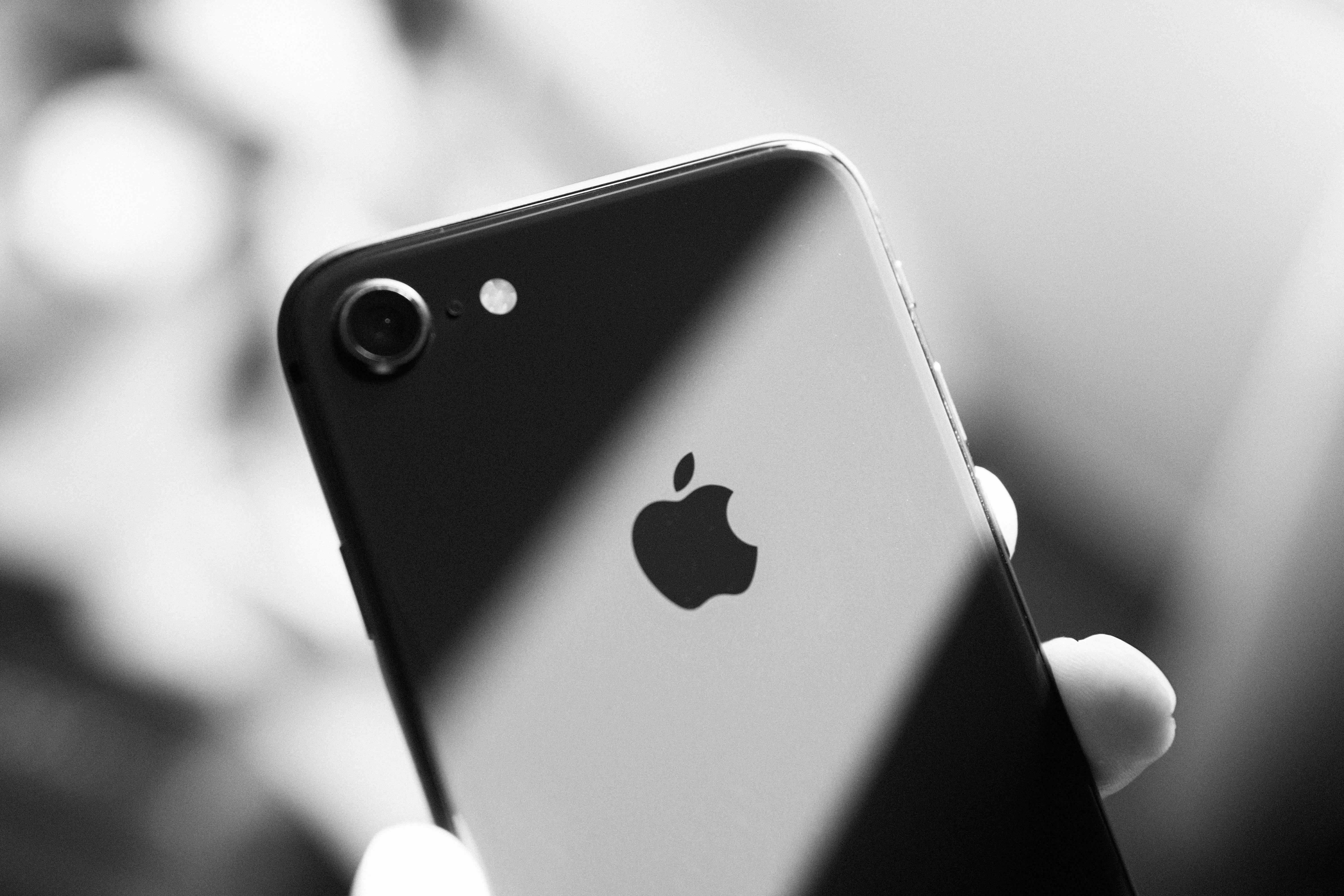 iPhone 8 灰階 壁紙 — 一隻手拿著iPhone的黑白特寫，Apple標誌和相機清晰可見。