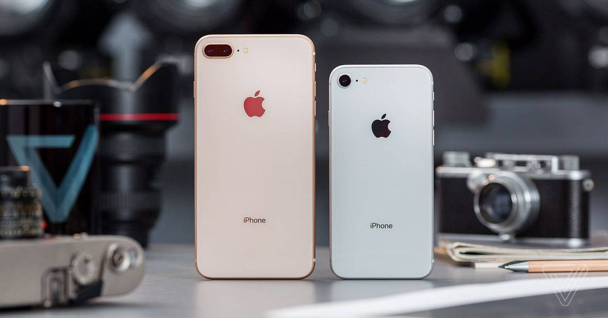 兩部金色和銀色的iPhone放在桌子上，配有復古相機和筆記本。