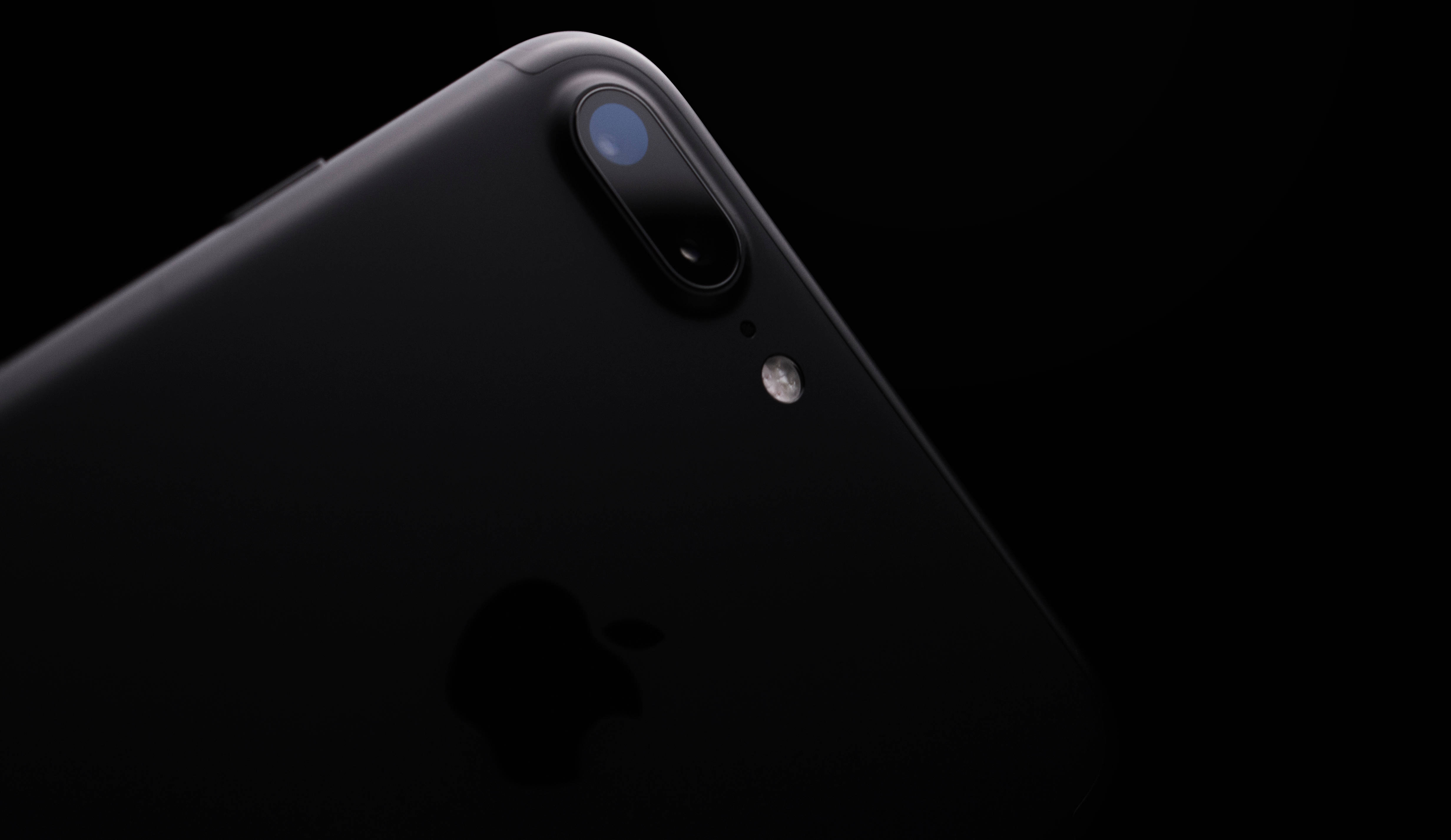 iPhone 8相機特寫 壁紙 — 一部時尚的黑色iPhone，配備雙攝像頭鏡頭和閃光燈，在純黑色背景上微微發光。