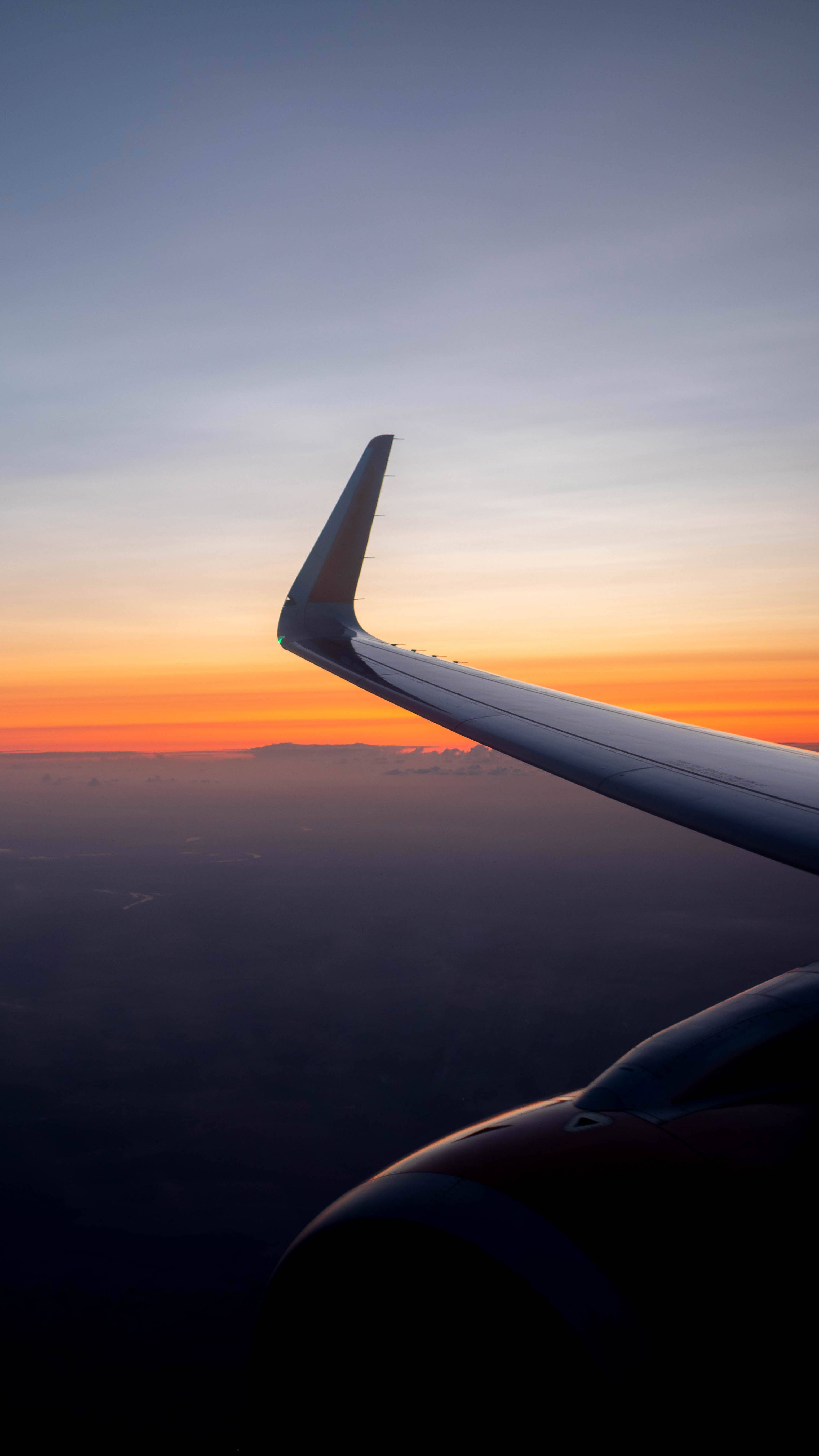 琥珀色天空飛機 iPhone 壁紙 — 飛機機翼在雲層上以鮮豔的橙色和紫色日落為背景的剪影。