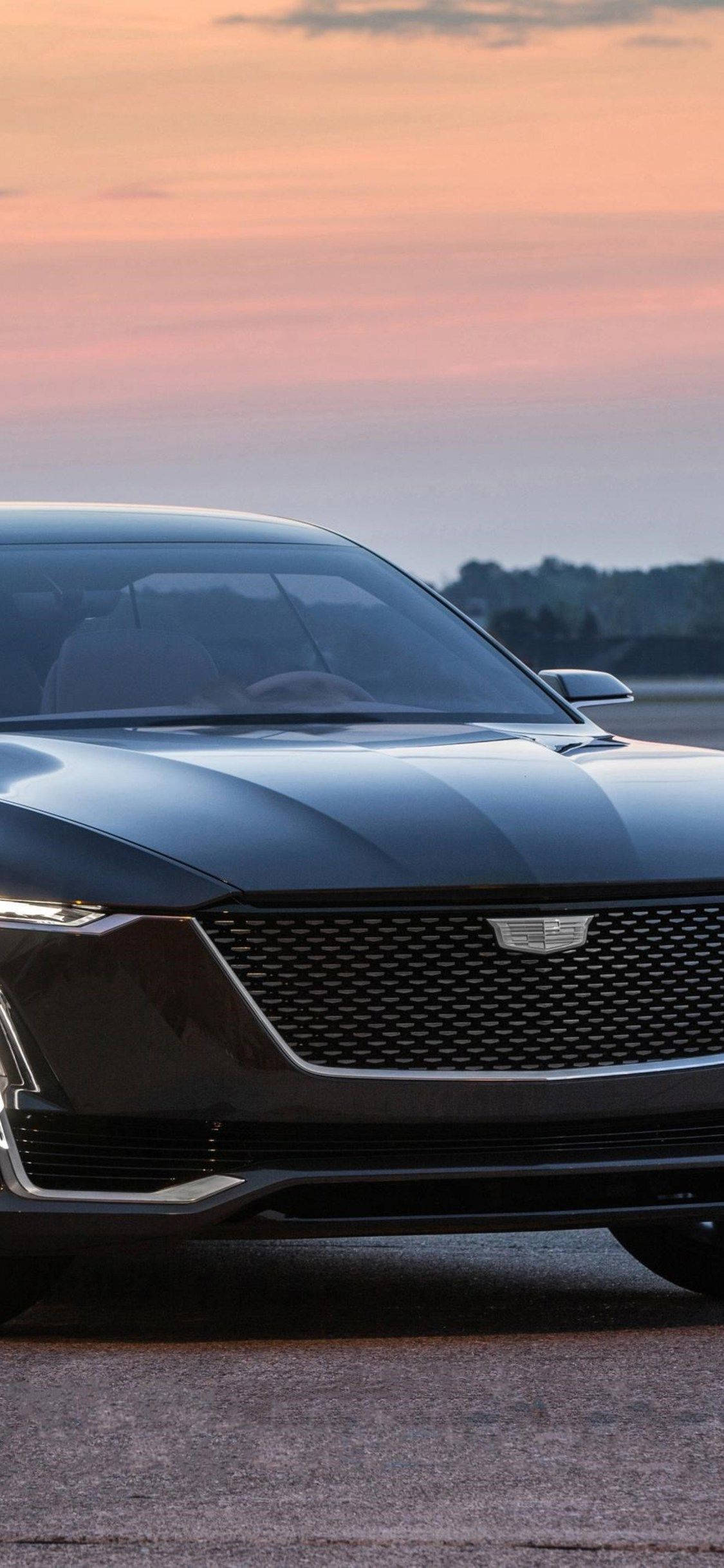 iPhone 拍攝的日落時分 Cadillac 壁紙 — 一輛時尚的黑色凱迪拉克轎車在柔和的粉紅色和橙色日落天空下閃閃發光，遠處有樹木。